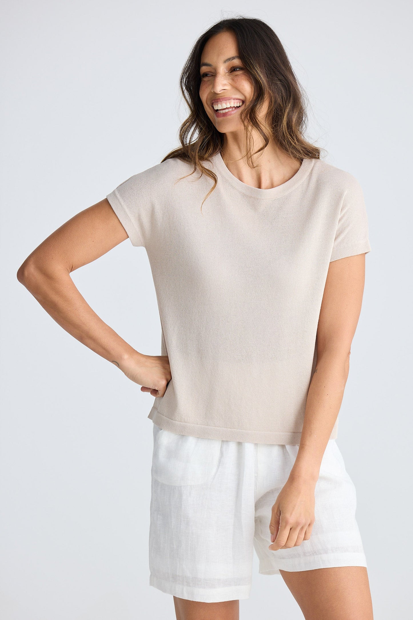 Woman wearing a beige top and white shorts on a plain background