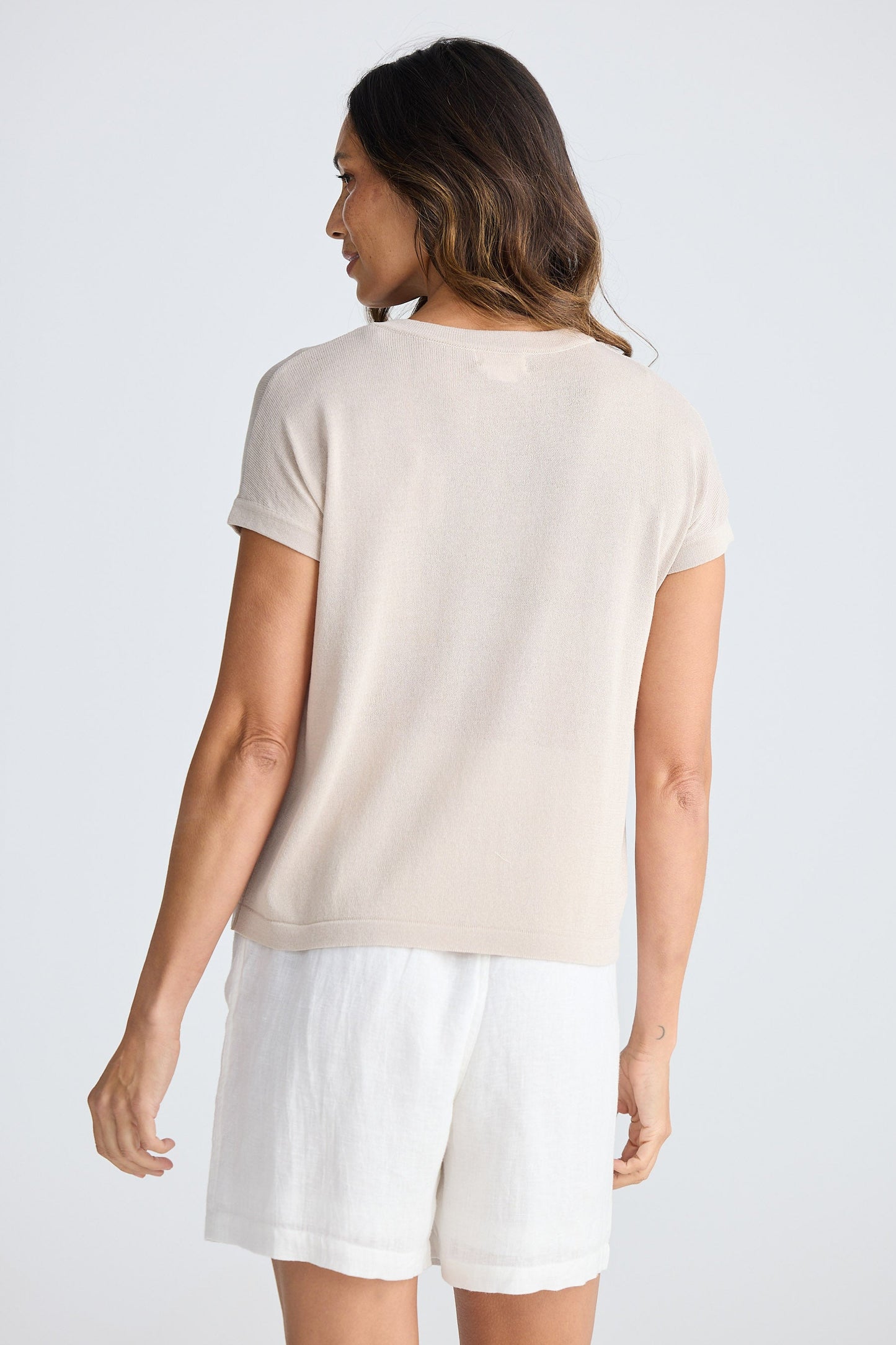 Woman wearing a beige t-shirt and white shorts on a plain background
