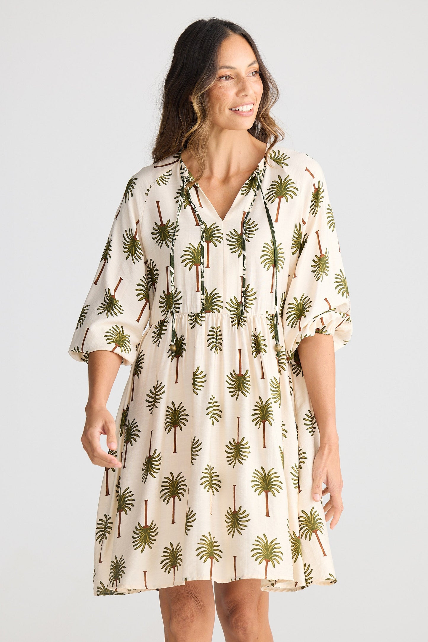 Woman wearing a palm tree patterned dress on a plain background