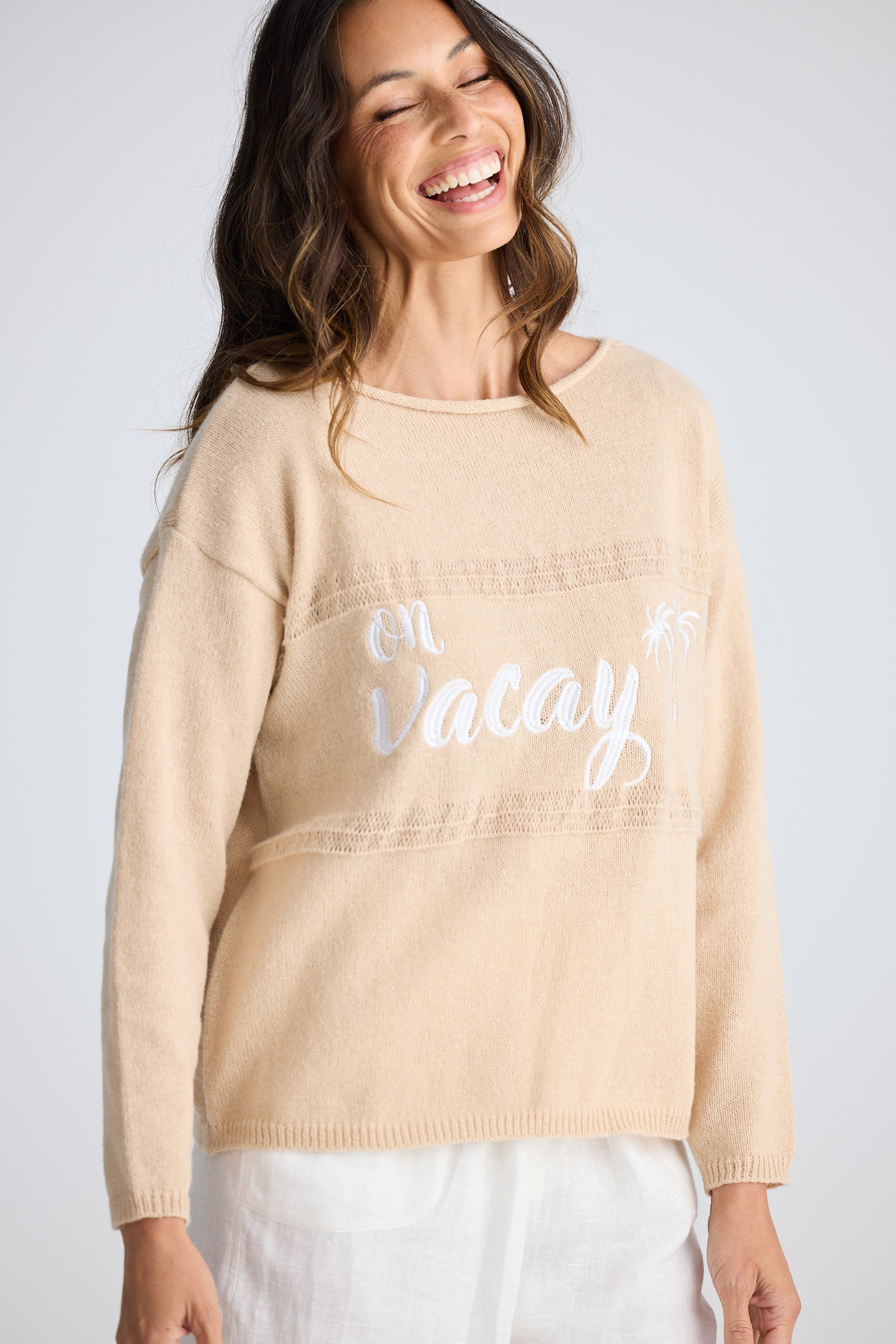 Woman wearing a beige sweater with 'On Vacay' text on a plain background