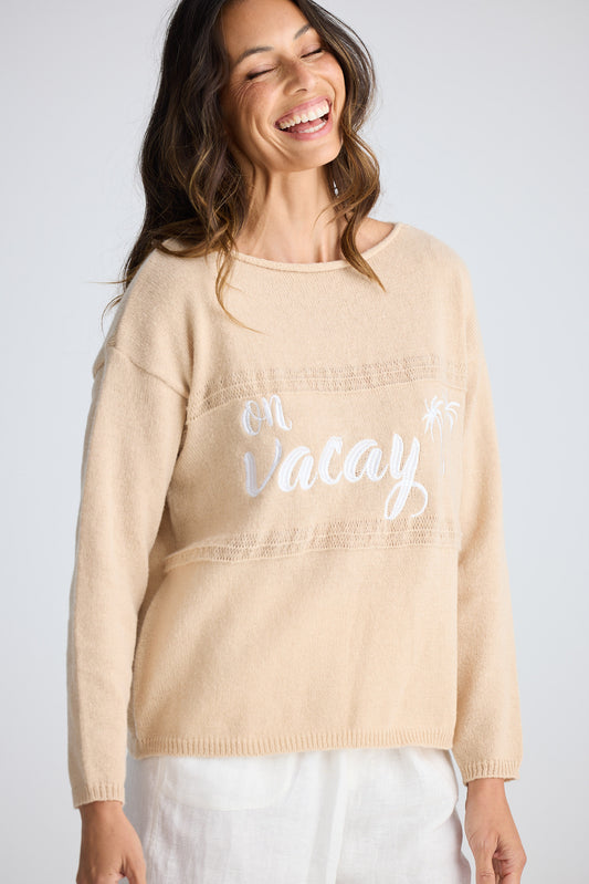 Woman wearing a beige sweater with 'On Vacay' text on a plain background