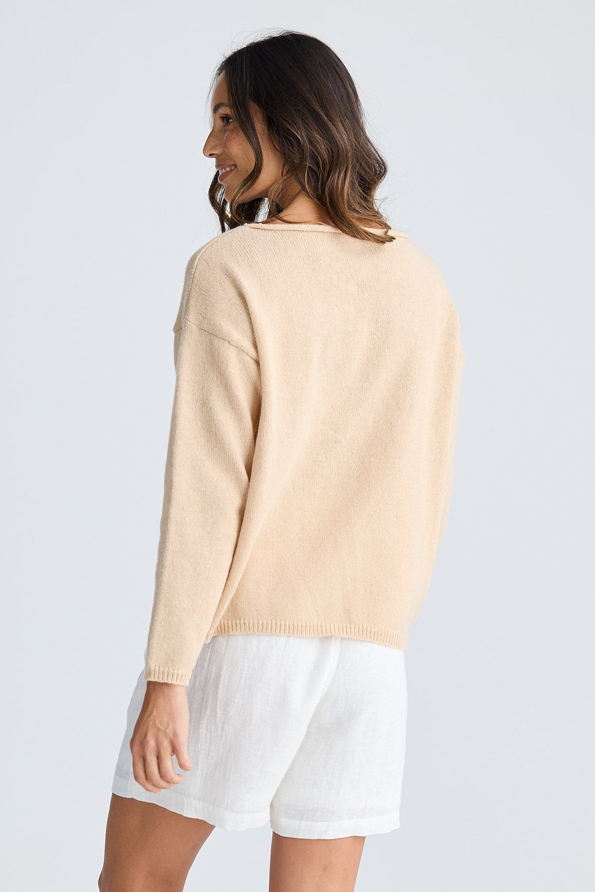 Woman wearing a beige sweater and white shorts on a light gray background