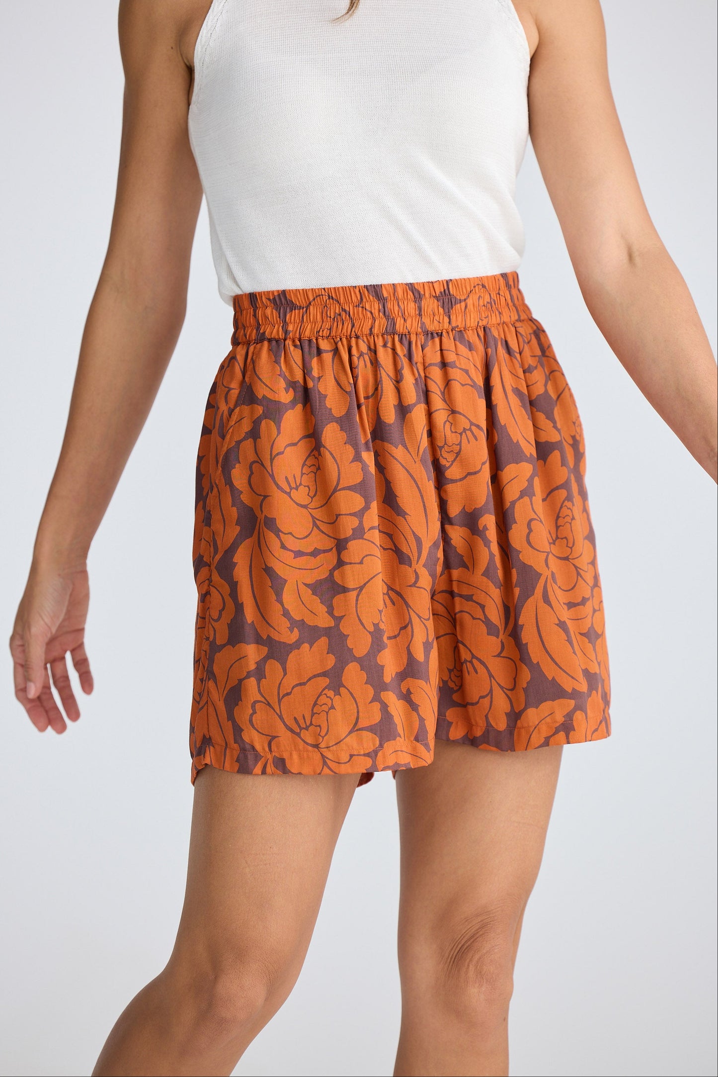 Person wearing orange floral shorts on a white background