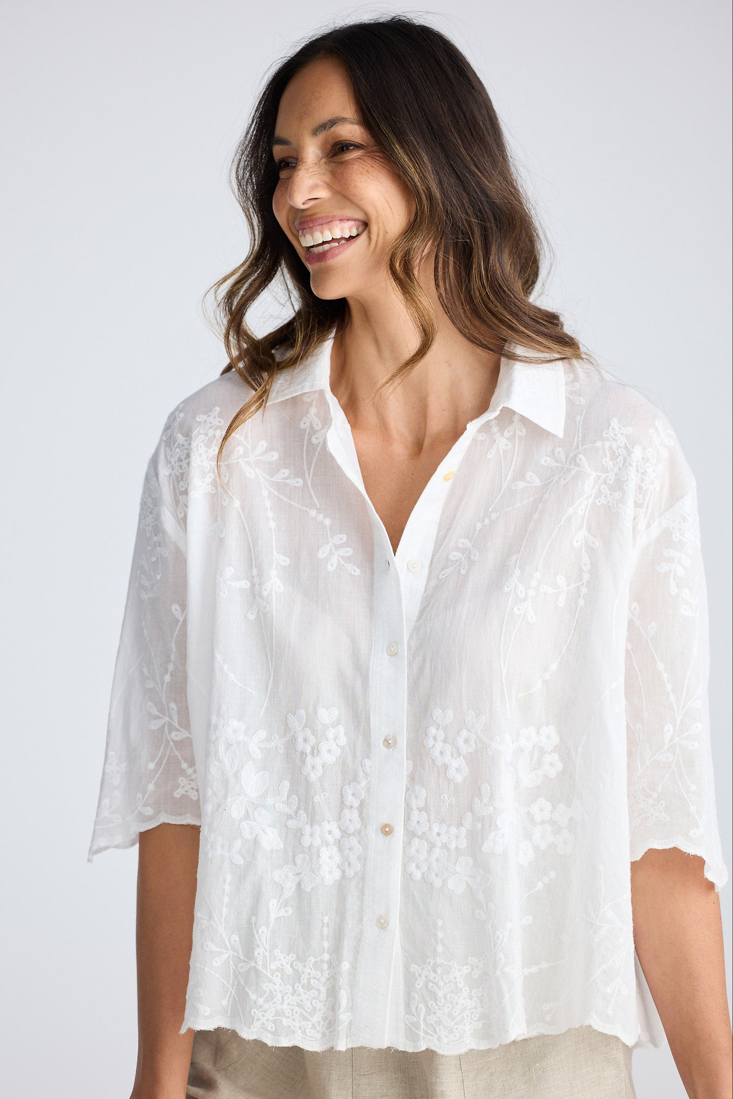 Woman wearing a white embroidered shirt against a plain background