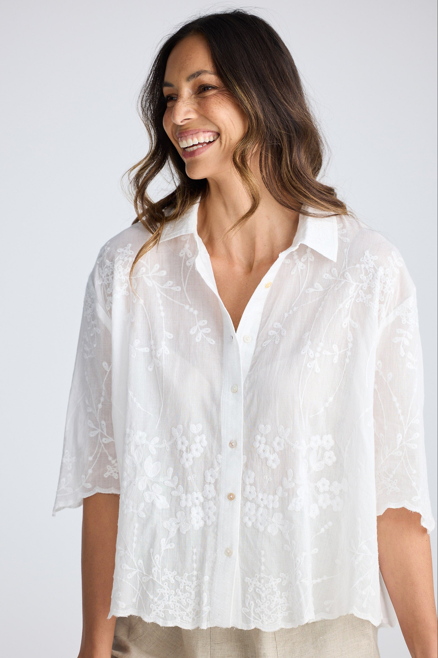 Woman wearing a white embroidered shirt against a plain background