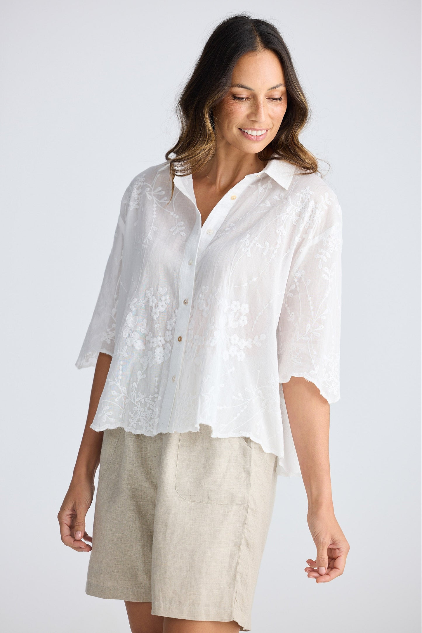 Woman wearing a white shirt and beige shorts on a plain background