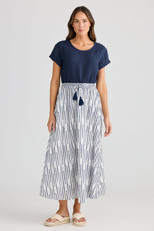 Woman wearing a navy top and white patterned skirt on a light gray background