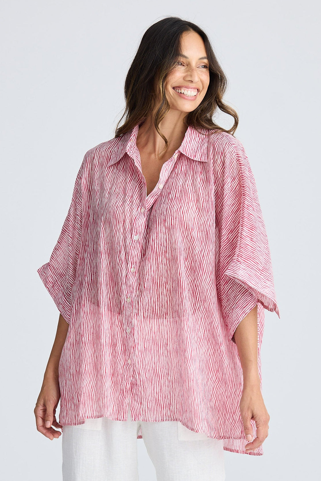 Woman wearing a pink striped shirt and white pants on a light gray background