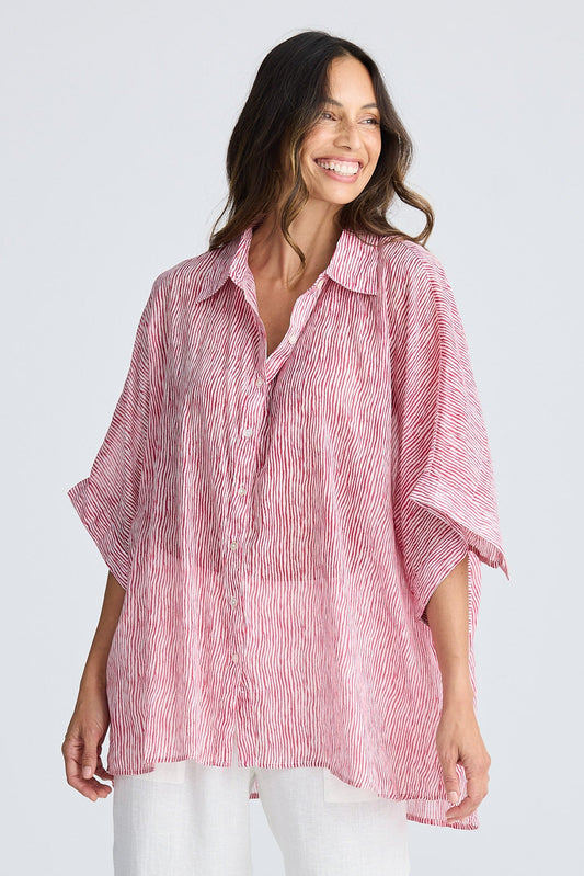 Woman wearing a pink striped shirt and white pants on a light gray background