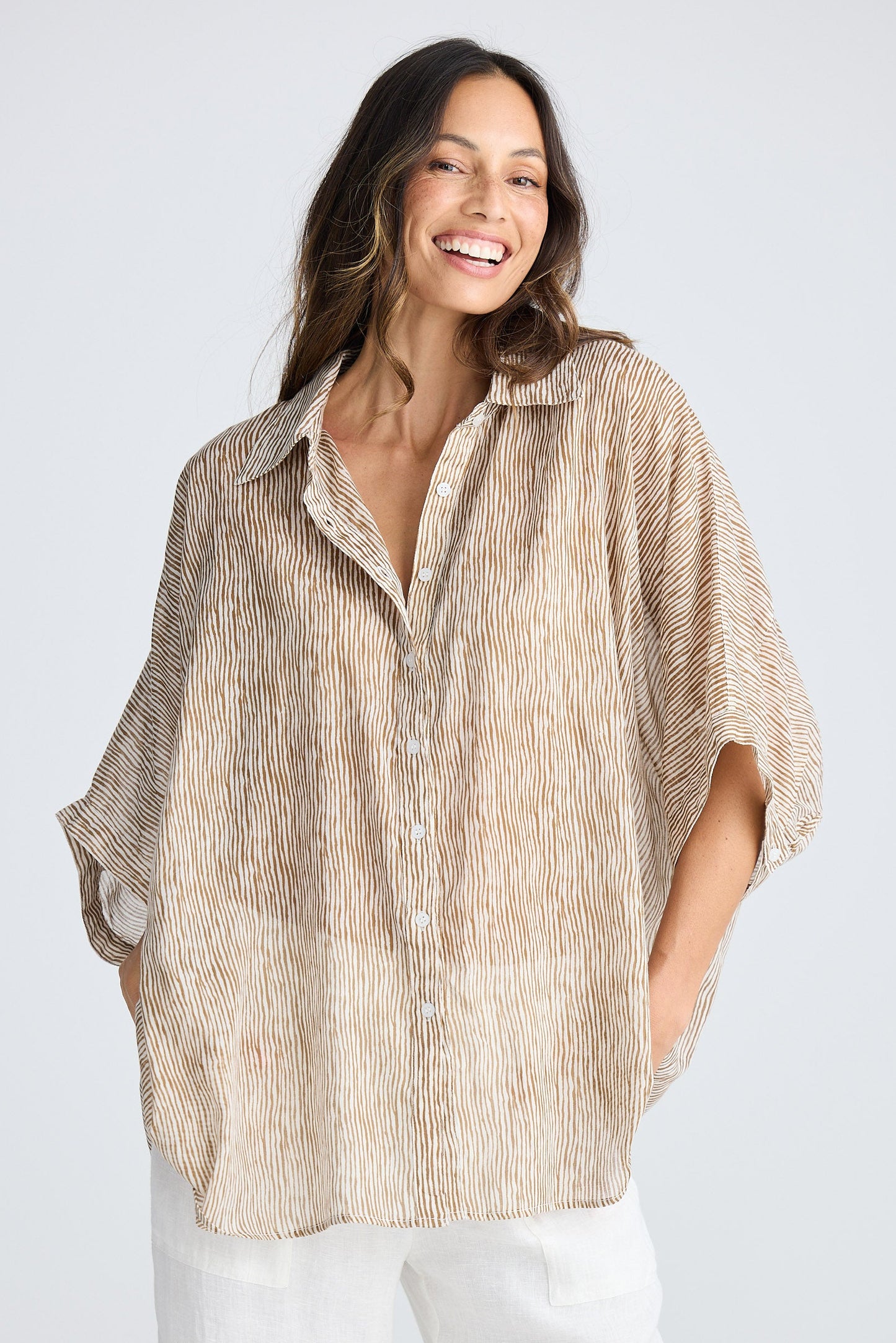 Woman wearing a beige patterned shirt and white pants on a white background