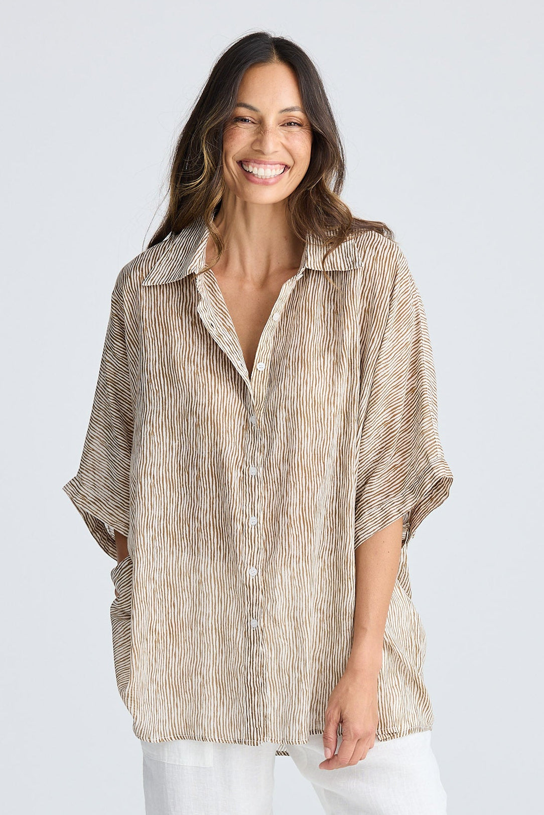 Woman wearing a beige shirt and white pants on a white background