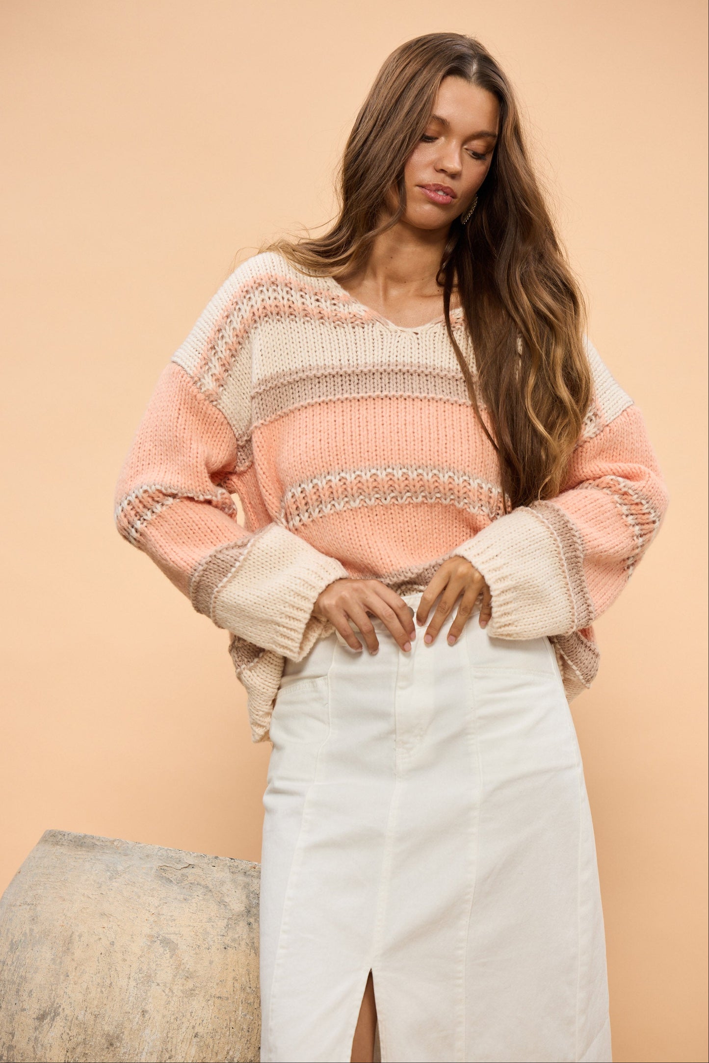 Woman in a striped sweater and white skirt standing next to a large pot on a beige background