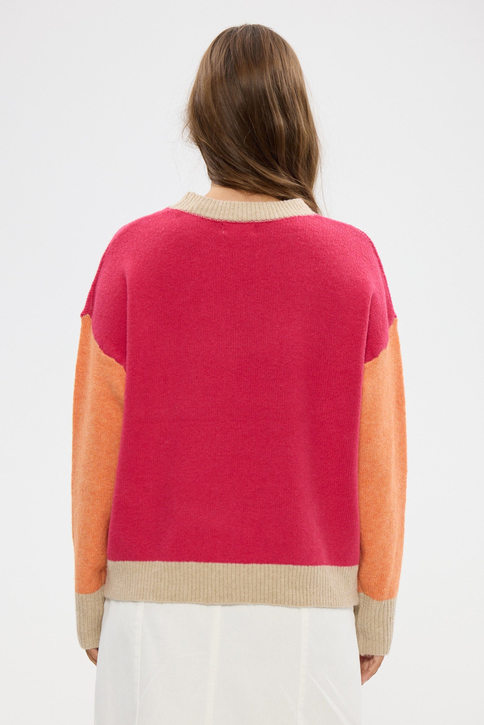 Woman wearing a color-blocked sweater with pink, orange, and beige sections on a white background