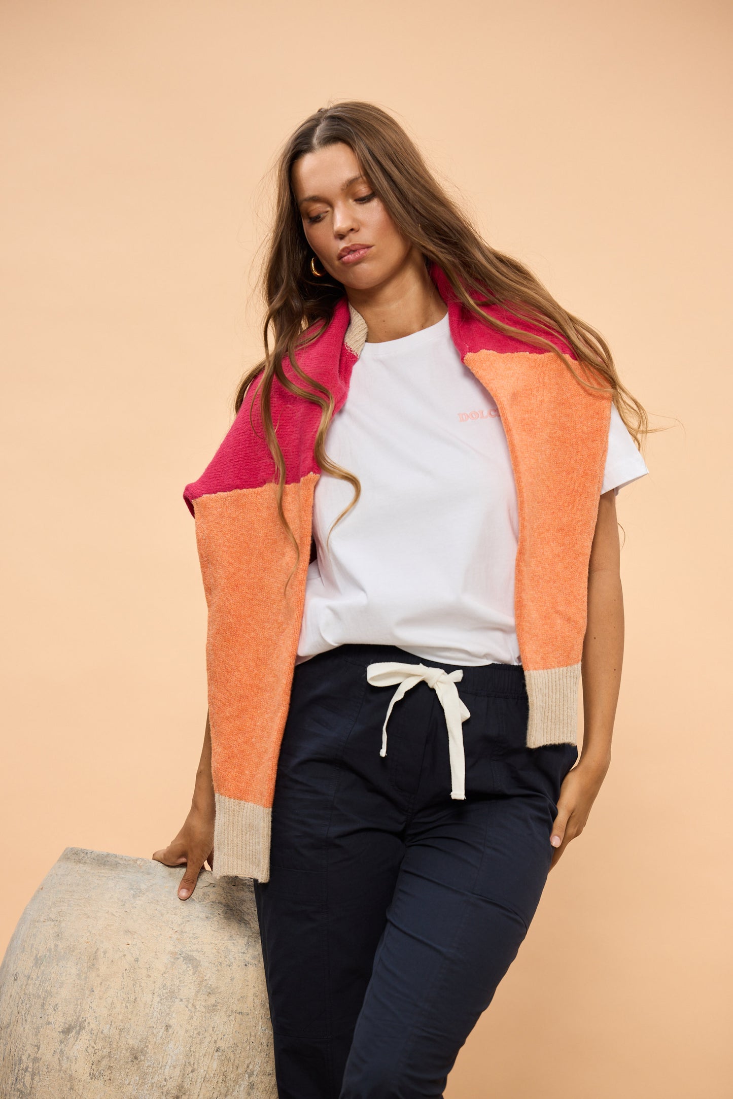 Woman wearing Navy Pants, White Tshirt with colourful jumper over shoulders with beige background