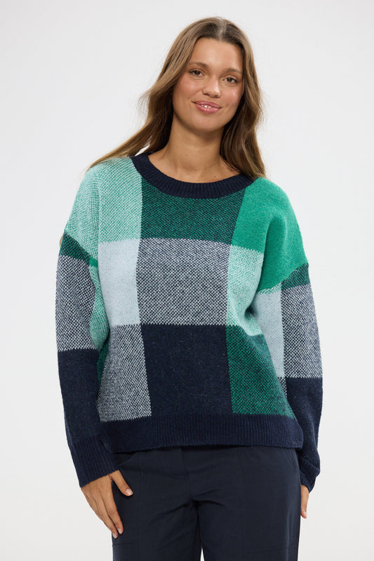 Woman wearing a checkered sweater with green, blue, and gray blocks on a white background