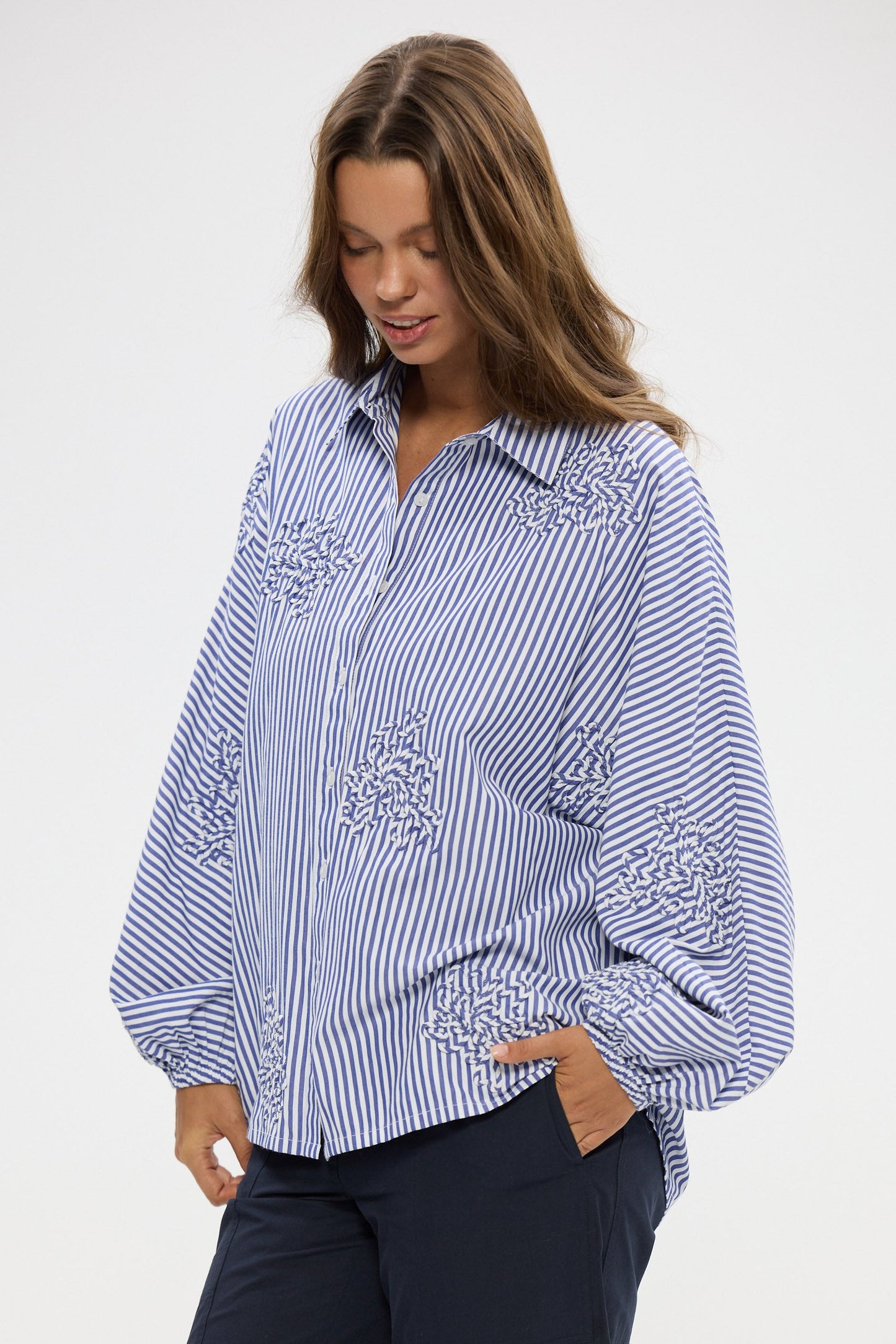 Woman wearing a blue and white striped shirt with embroidery on a white background