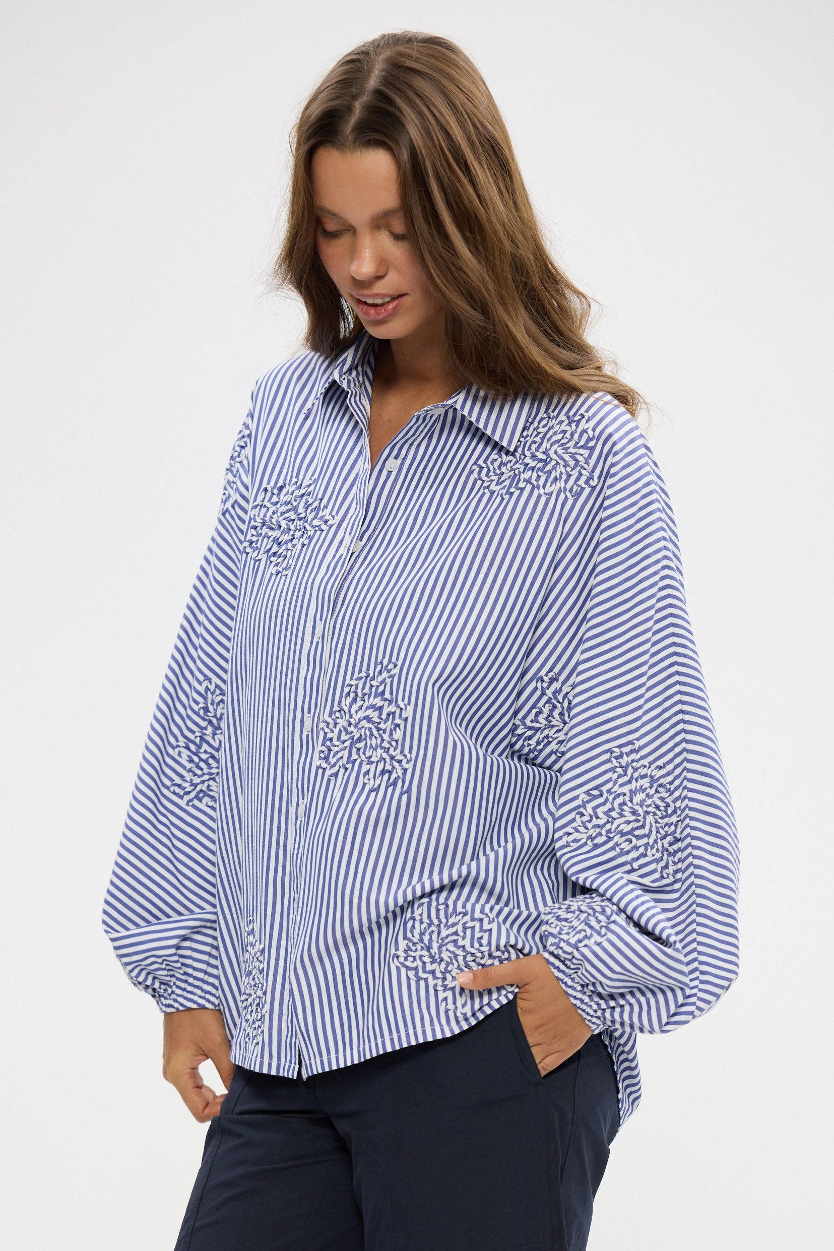 Woman wearing a blue and white striped shirt with embroidery on a white background