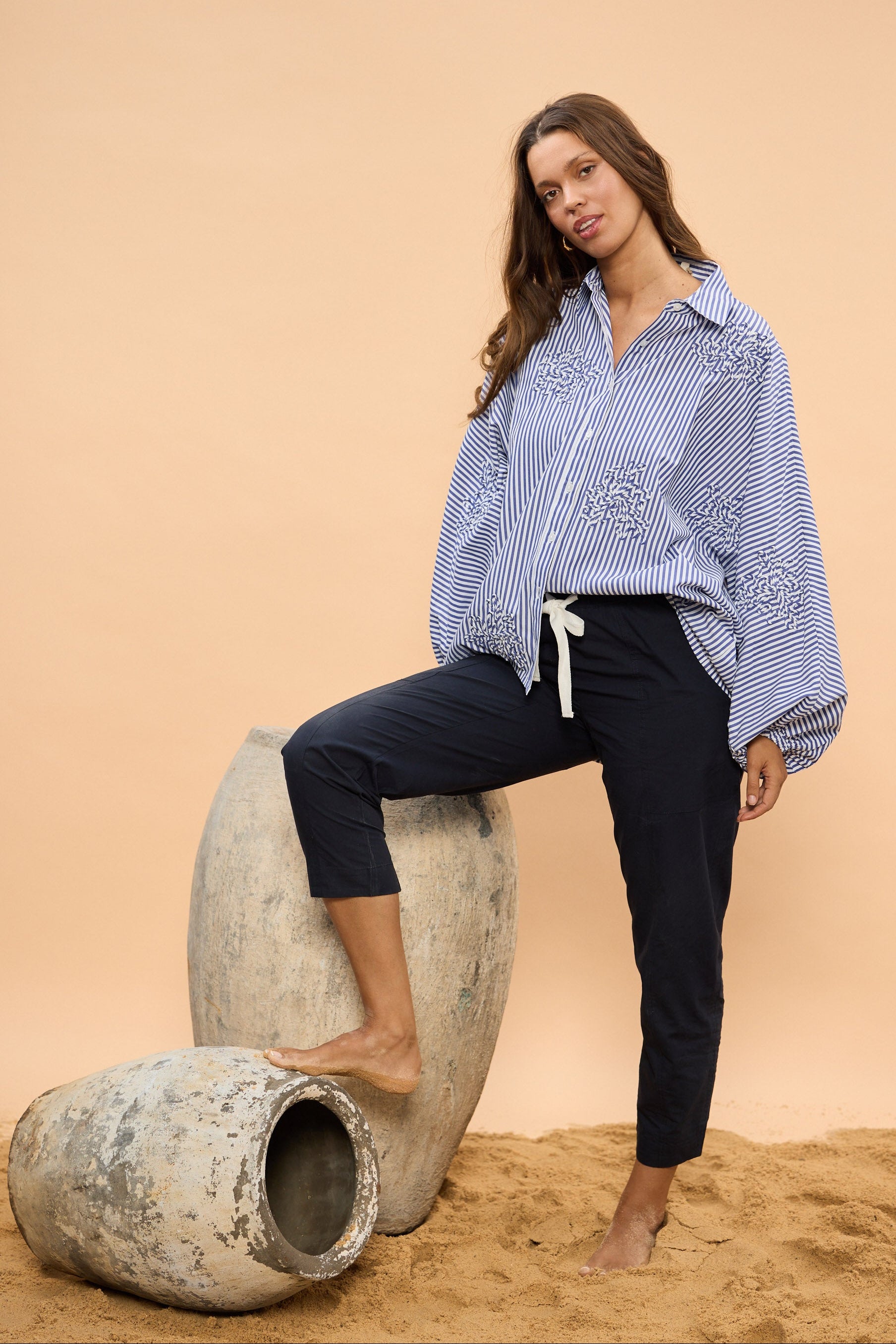 Woman in a blue and white striped shirt and navy pants standing on a beige background