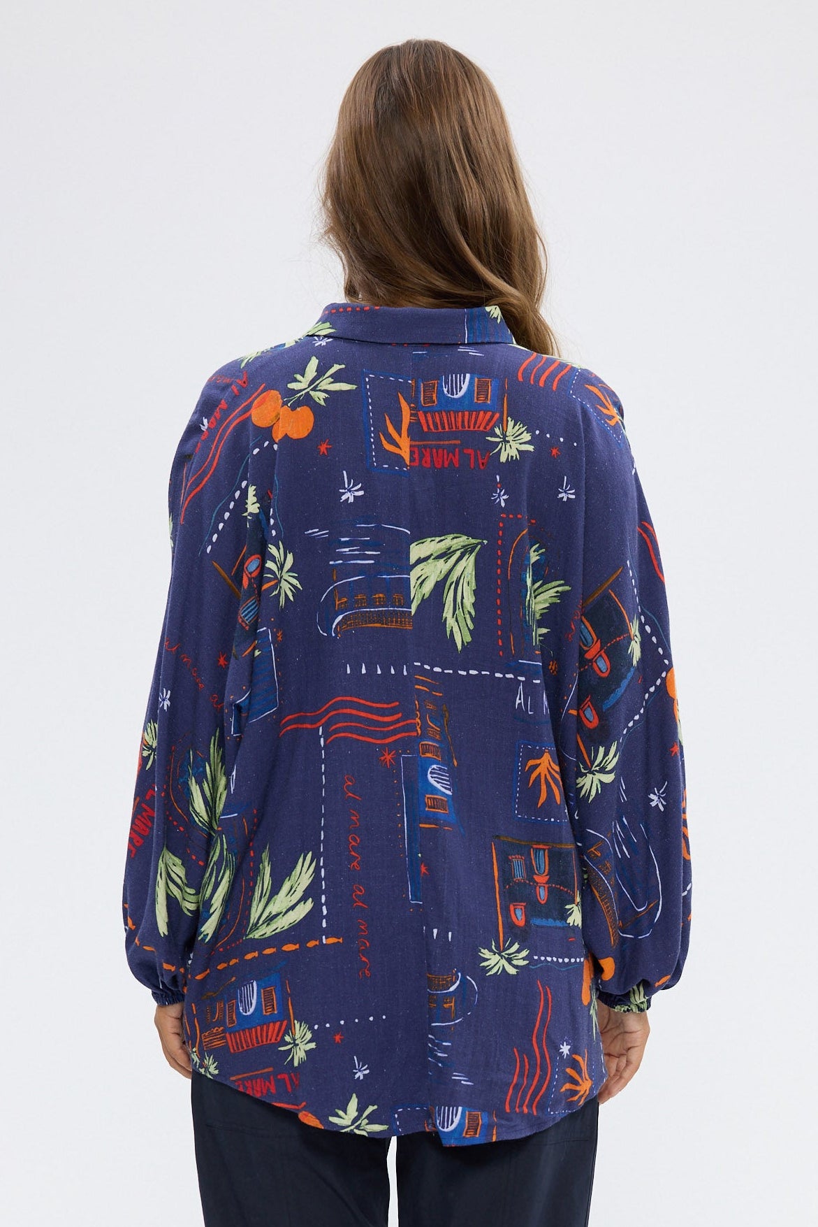 Woman wearing a colorful patterned shirt and dark pants on a white background