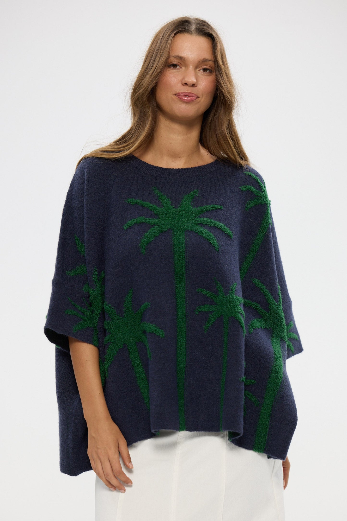 Woman wearing a navy blue poncho with green palm tree patterns on a white background