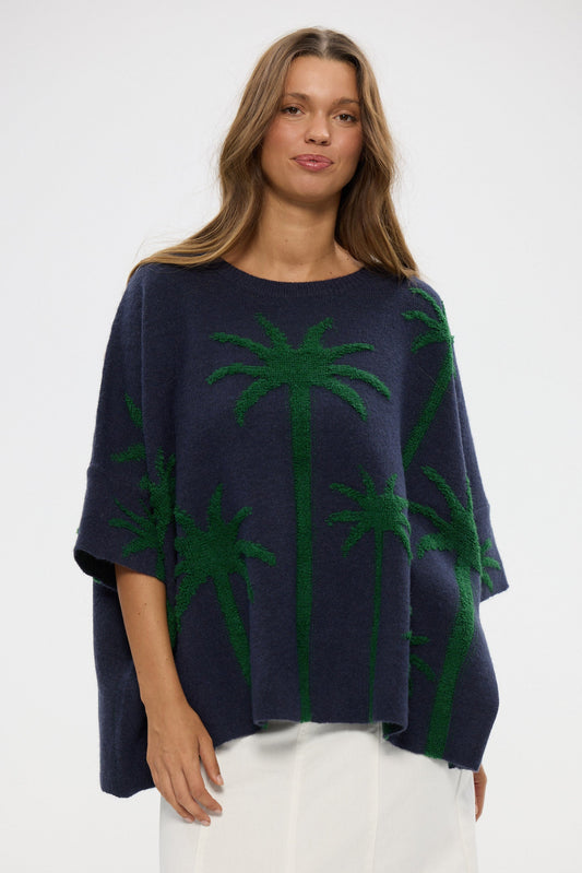 Woman wearing a navy blue poncho with green palm tree patterns on a white background