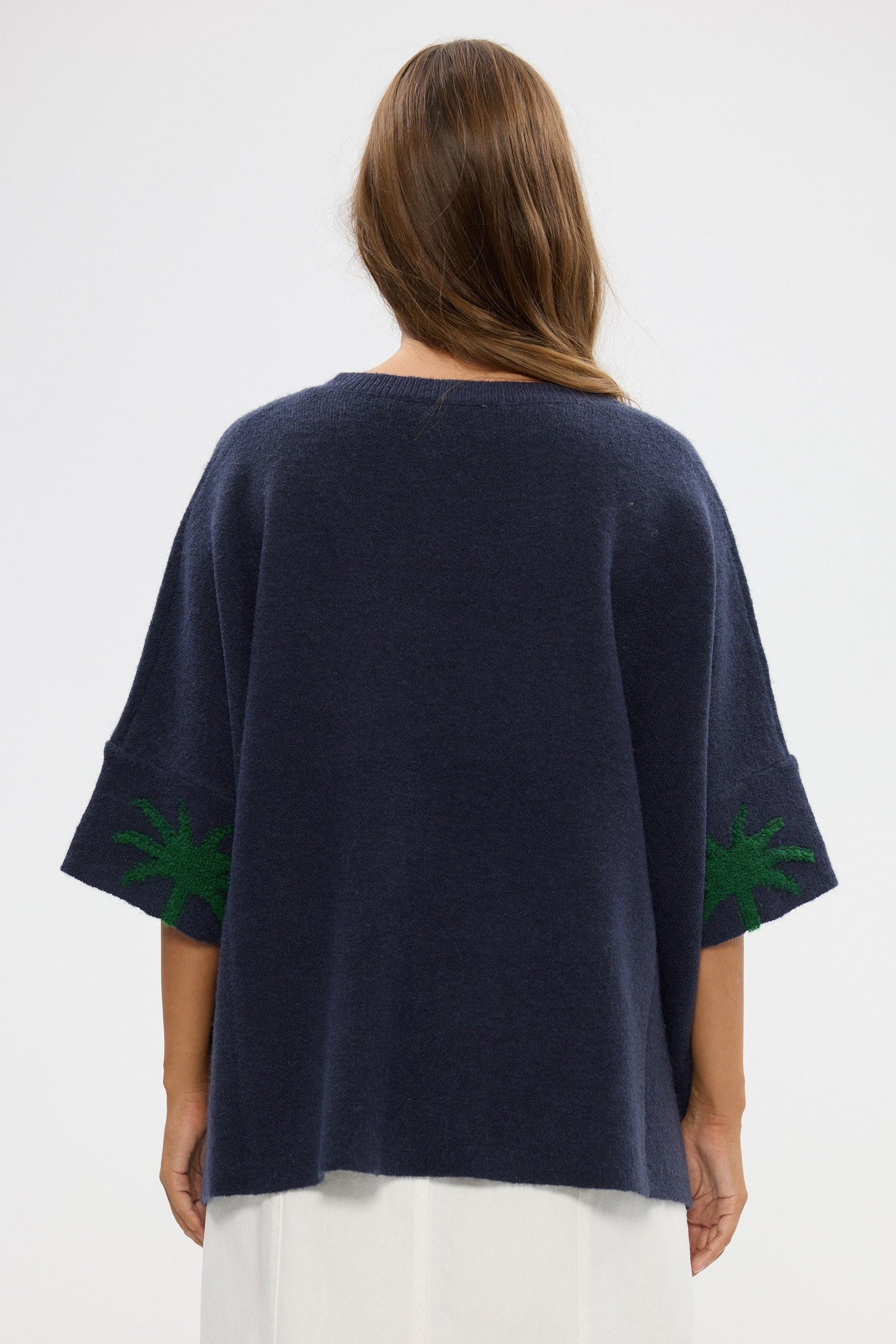 Navy blue top with green patterns on sleeves worn by a person on a white background