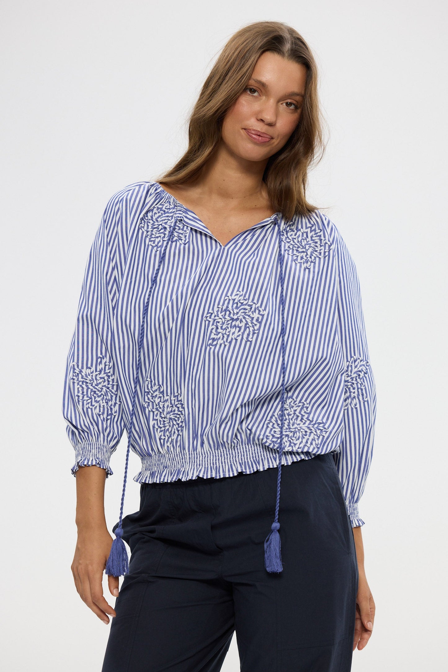 Woman wearing a blue and white striped blouse with embroidery, standing against a plain background