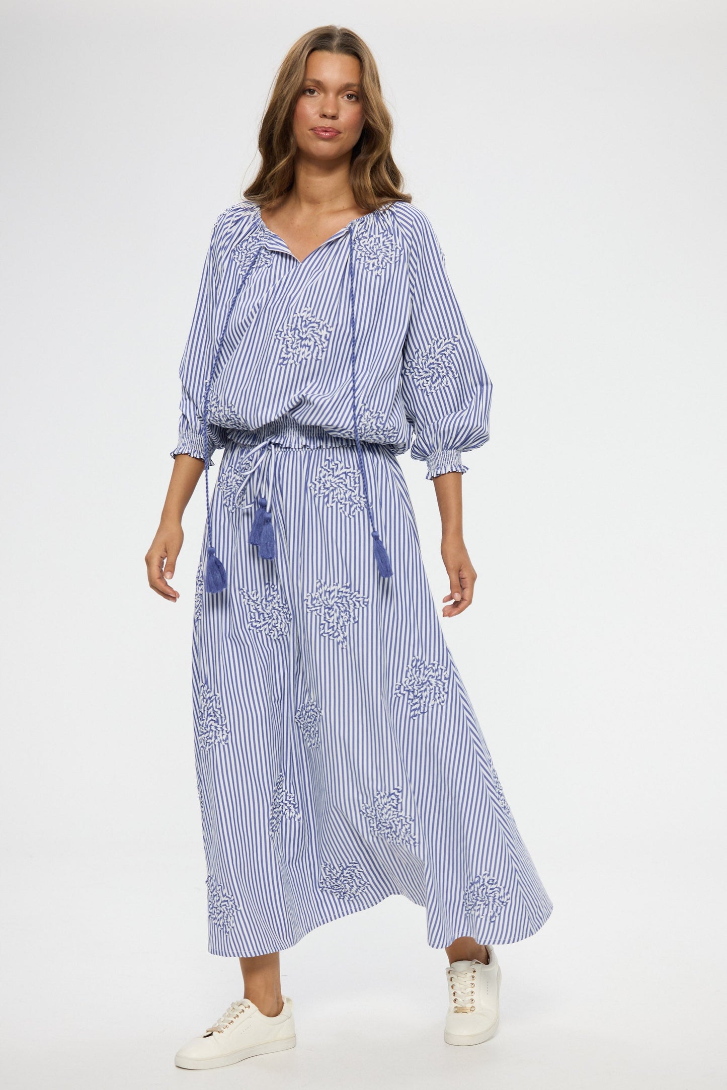 Woman wearing a blue and white striped top and skirt with floral embroidery on a white background