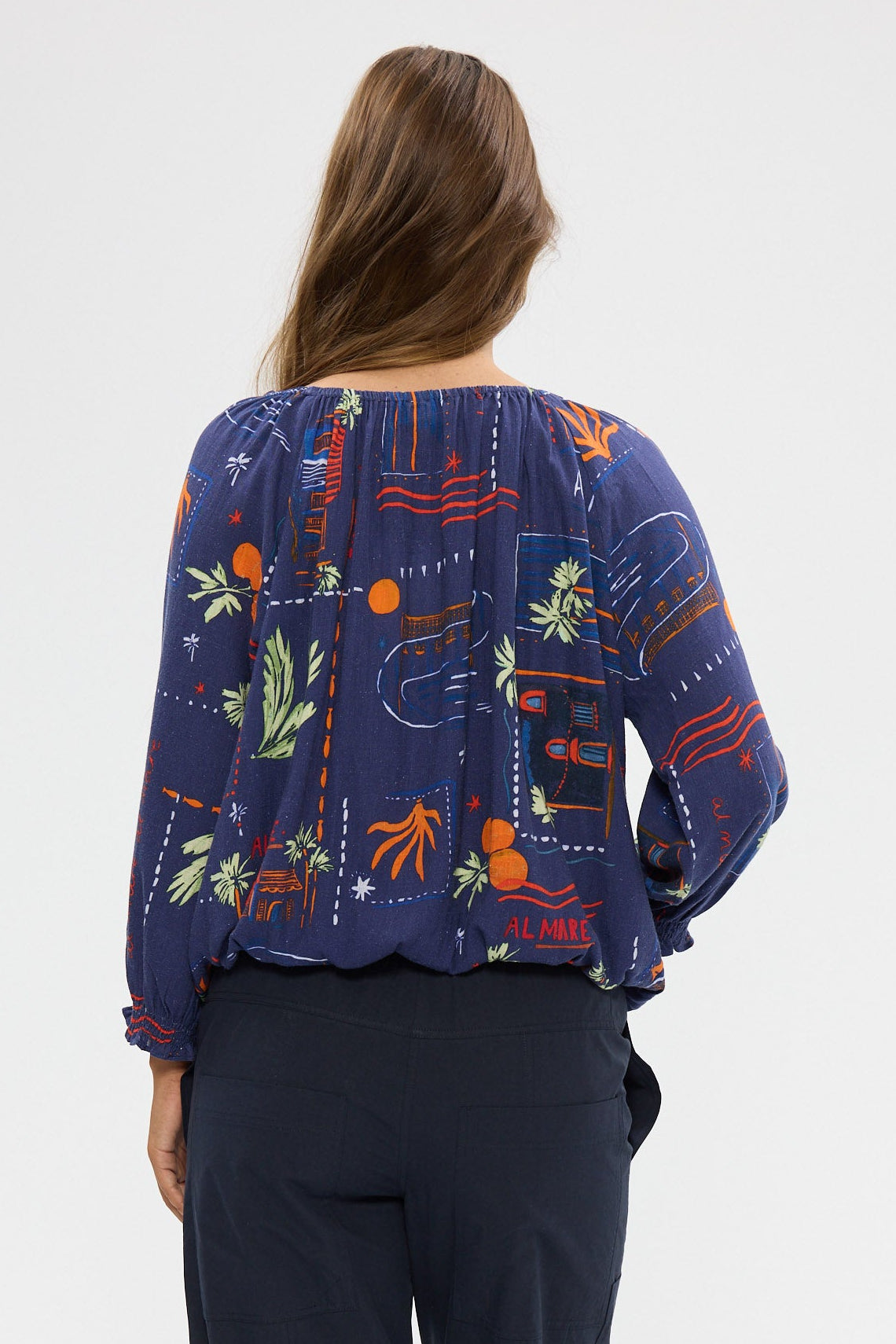 Woman wearing a blue patterned top and dark pants on a white background