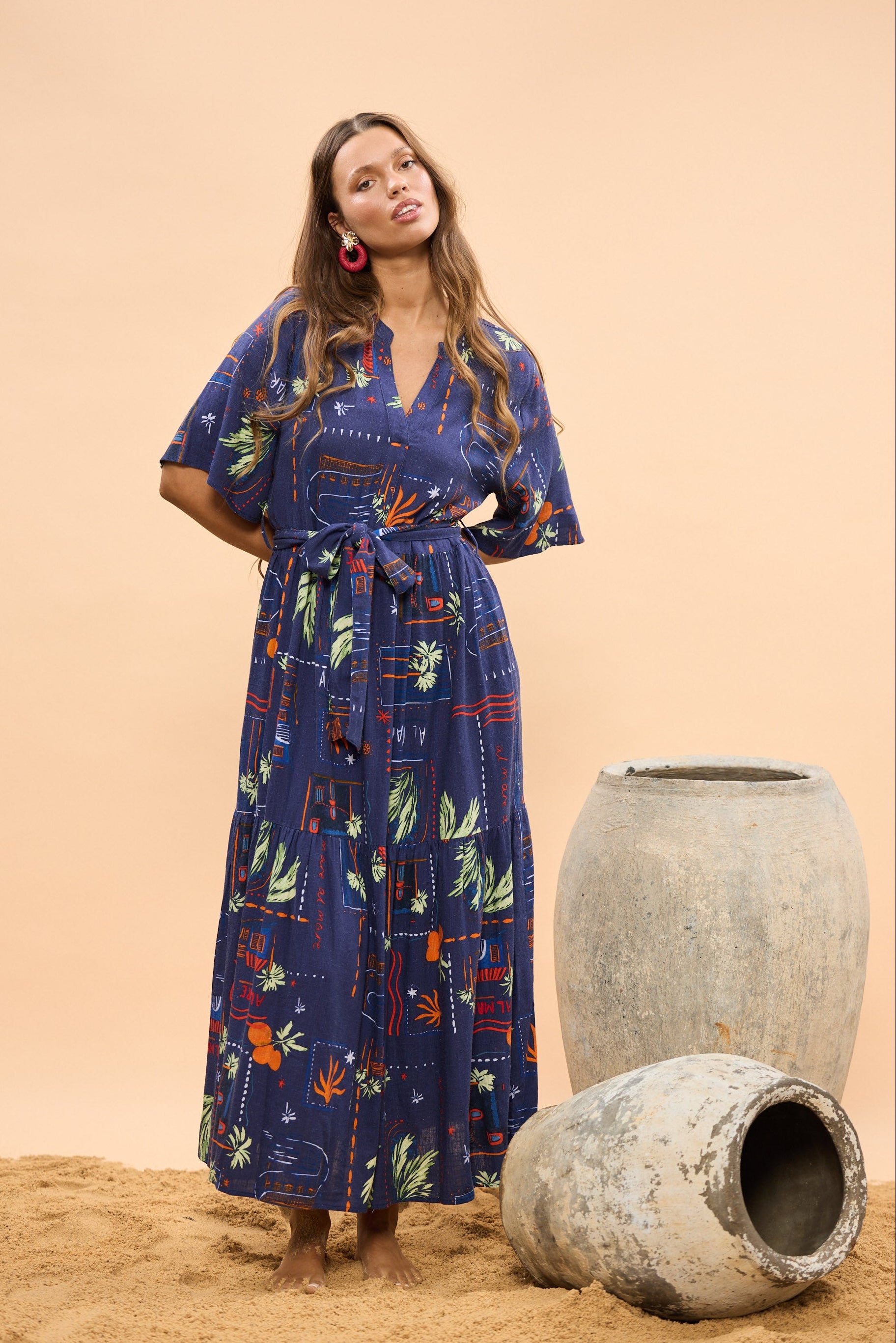 Woman in a long blue dress standing next to large stone pots on a beige background