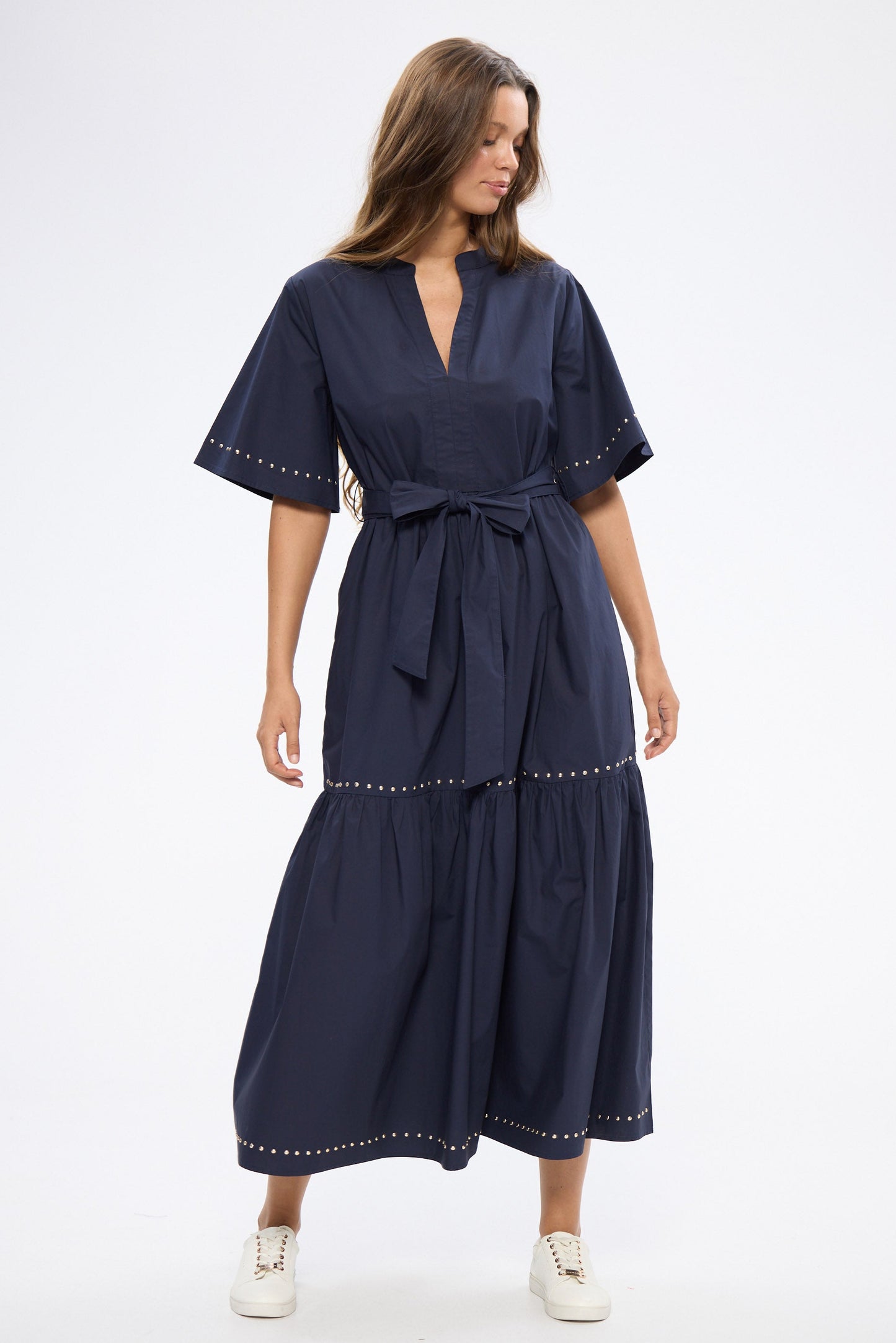 Woman wearing a navy dress with white shoes on a white background