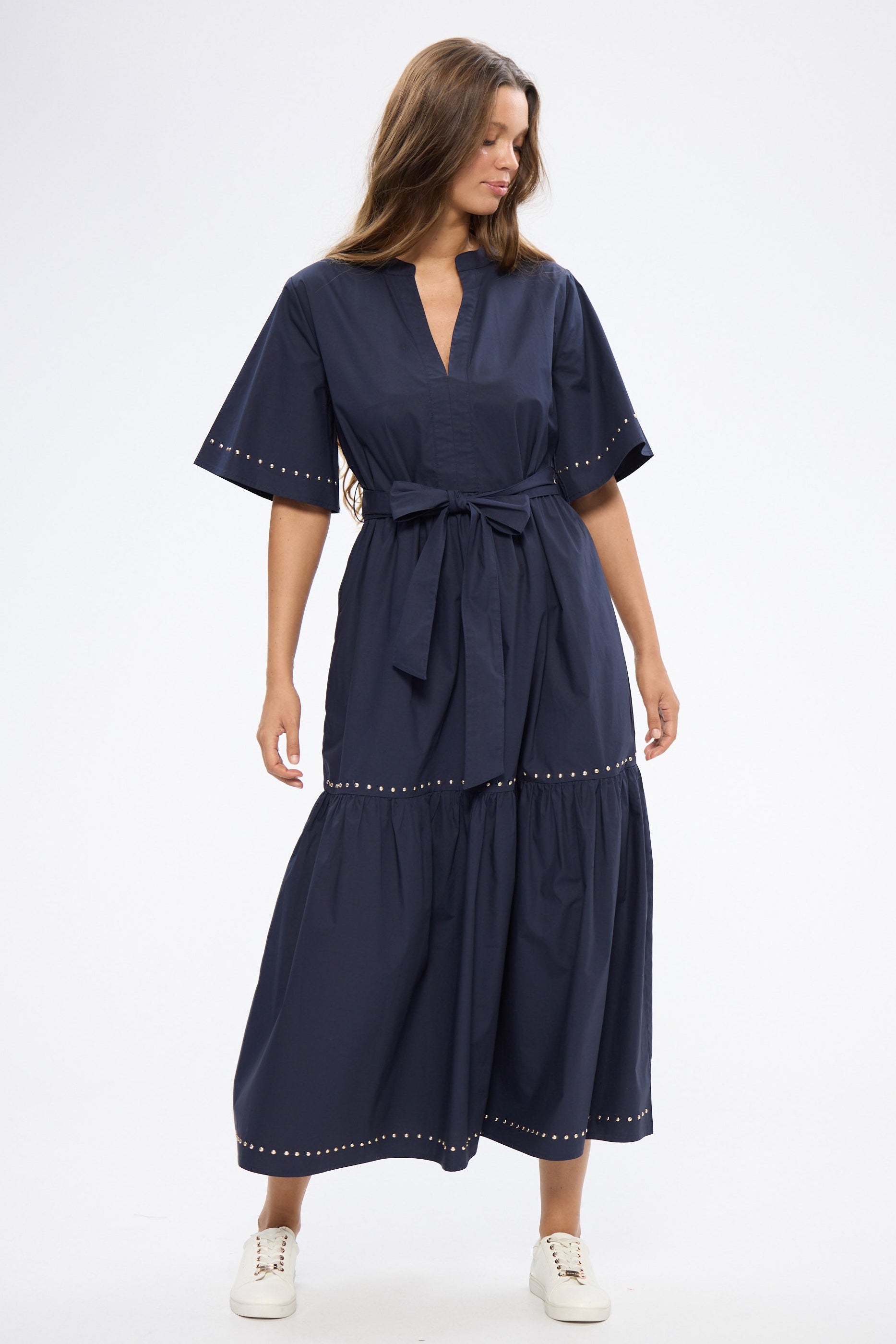 Woman wearing a navy dress with white shoes on a white background