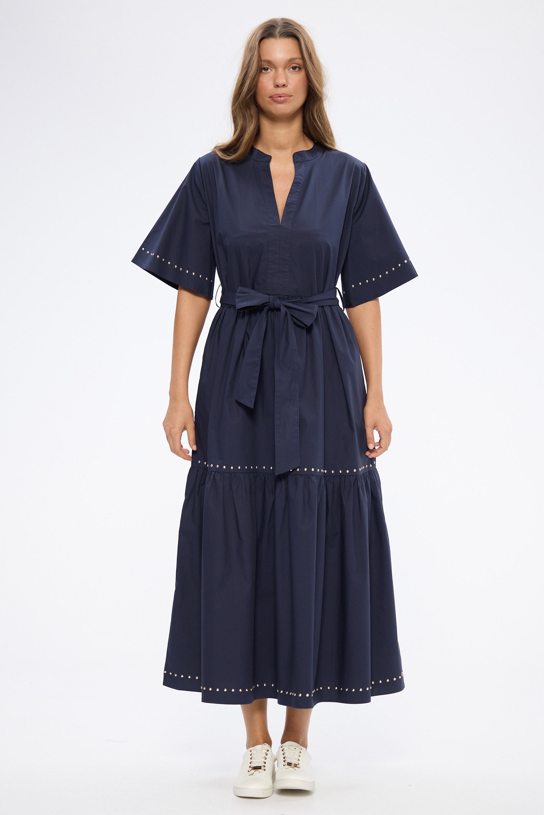 Woman wearing a navy dress with white shoes on a white background