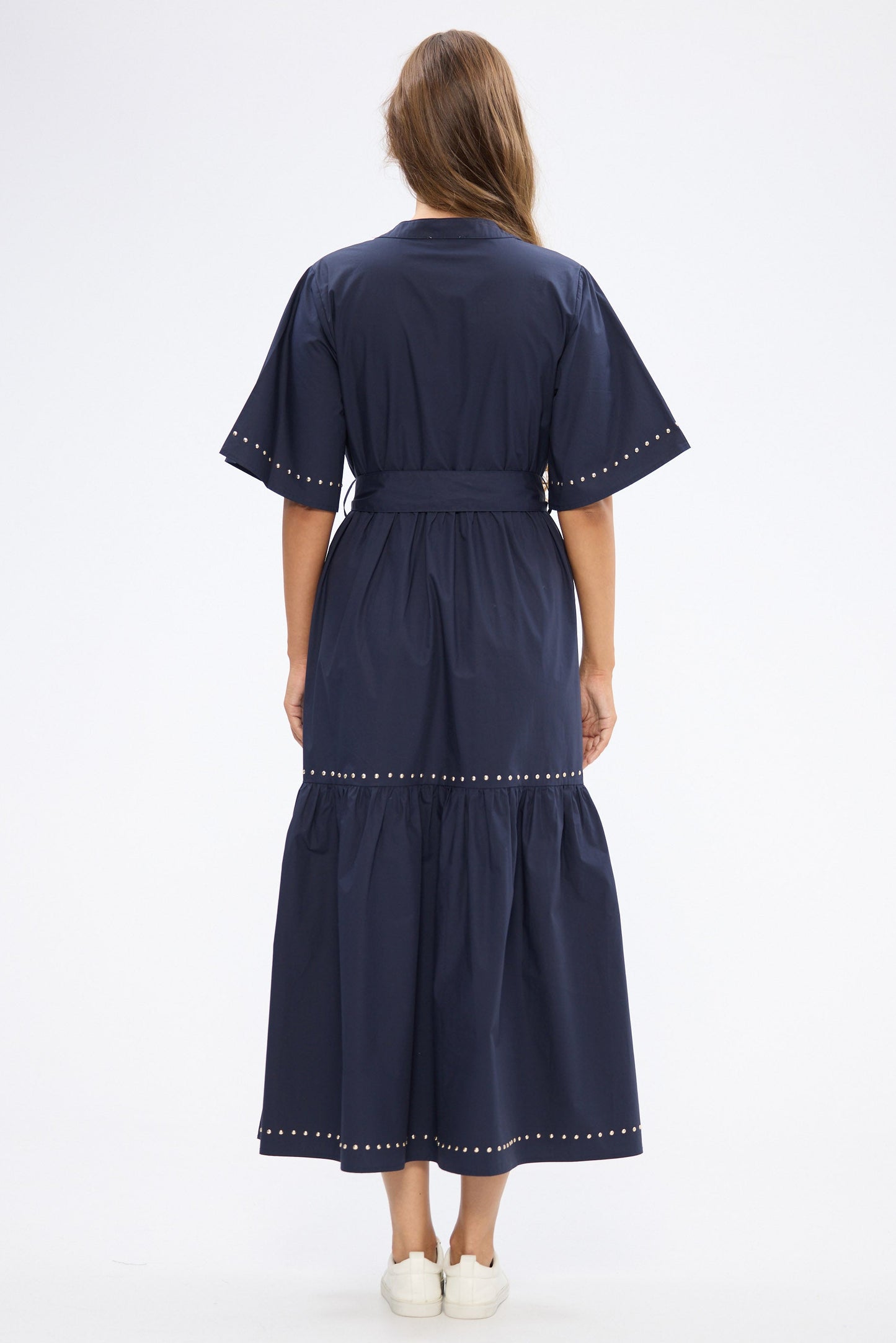 Woman wearing a navy dress with stud trim on a white background
