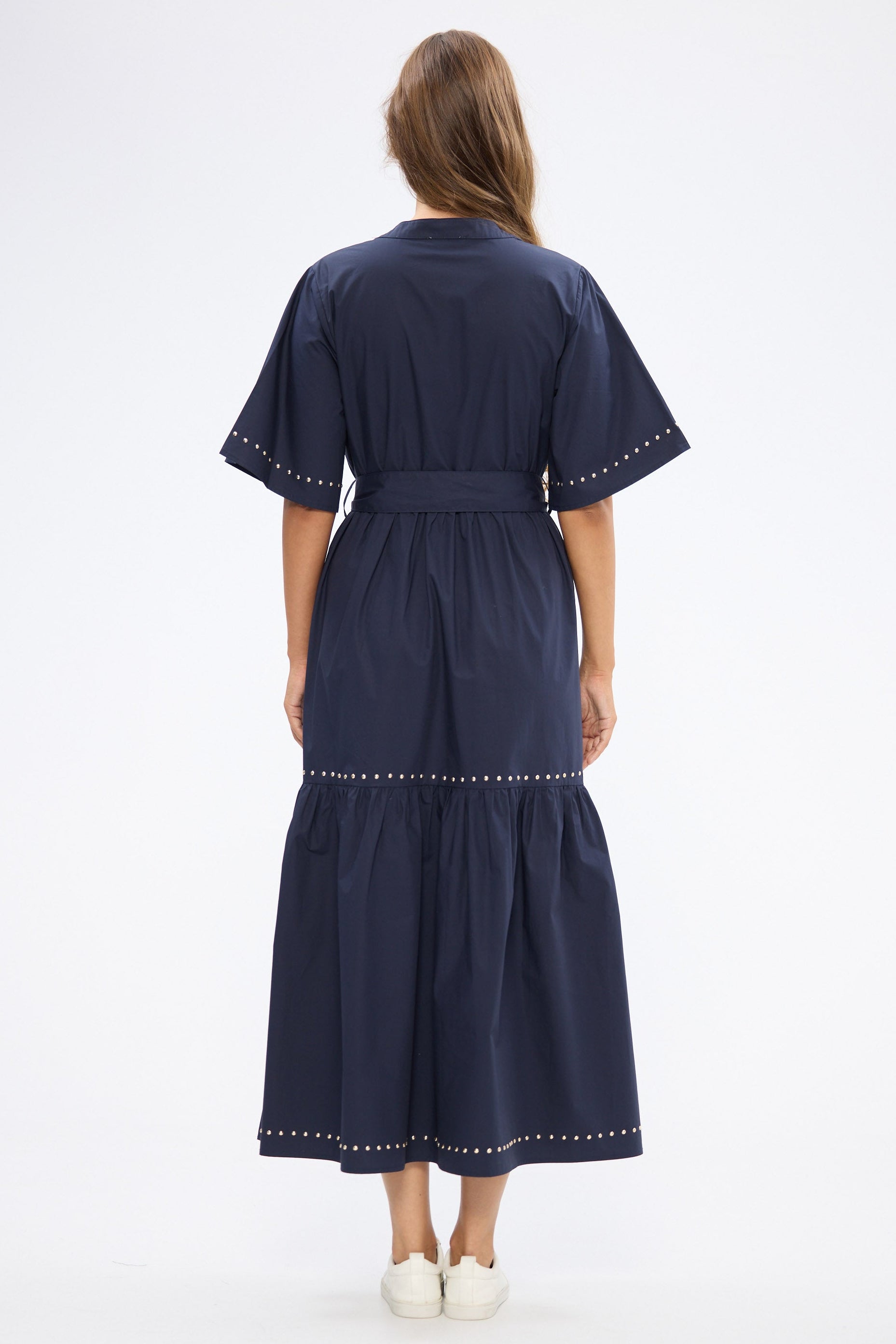 Woman wearing a navy dress with stud trim on a white background