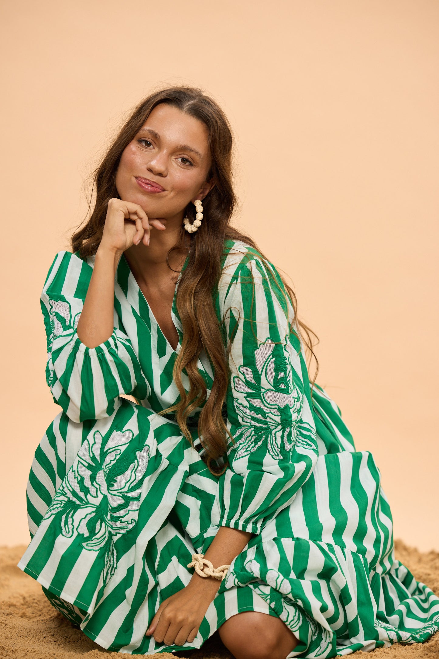 Woman wearing a green and white striped dress with floral patterns on a beige background