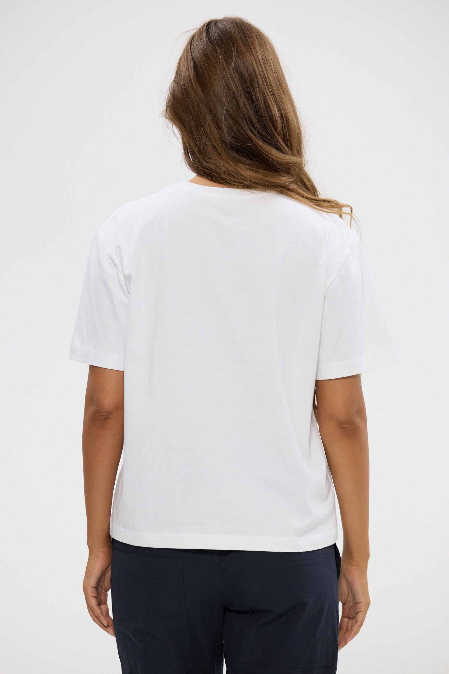 Person wearing a white t-shirt and dark pants on a plain background