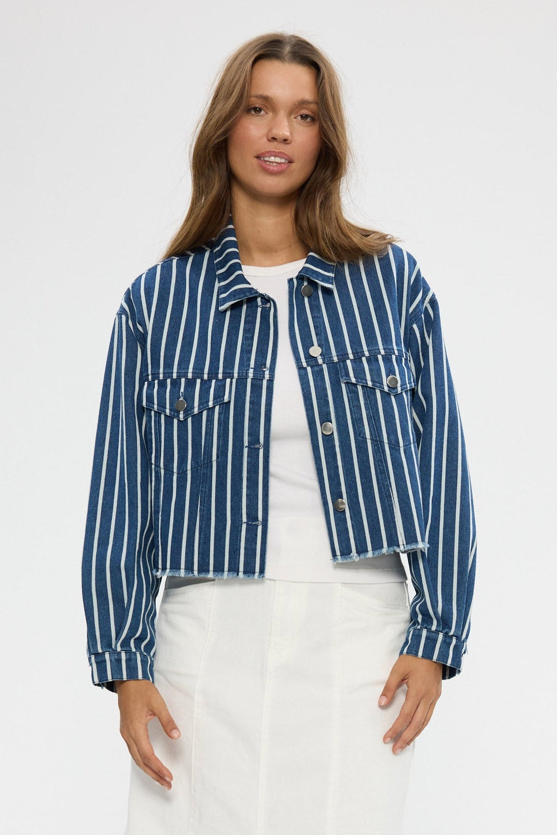 Woman wearing a blue striped jacket, white top, and white skirt on a white background