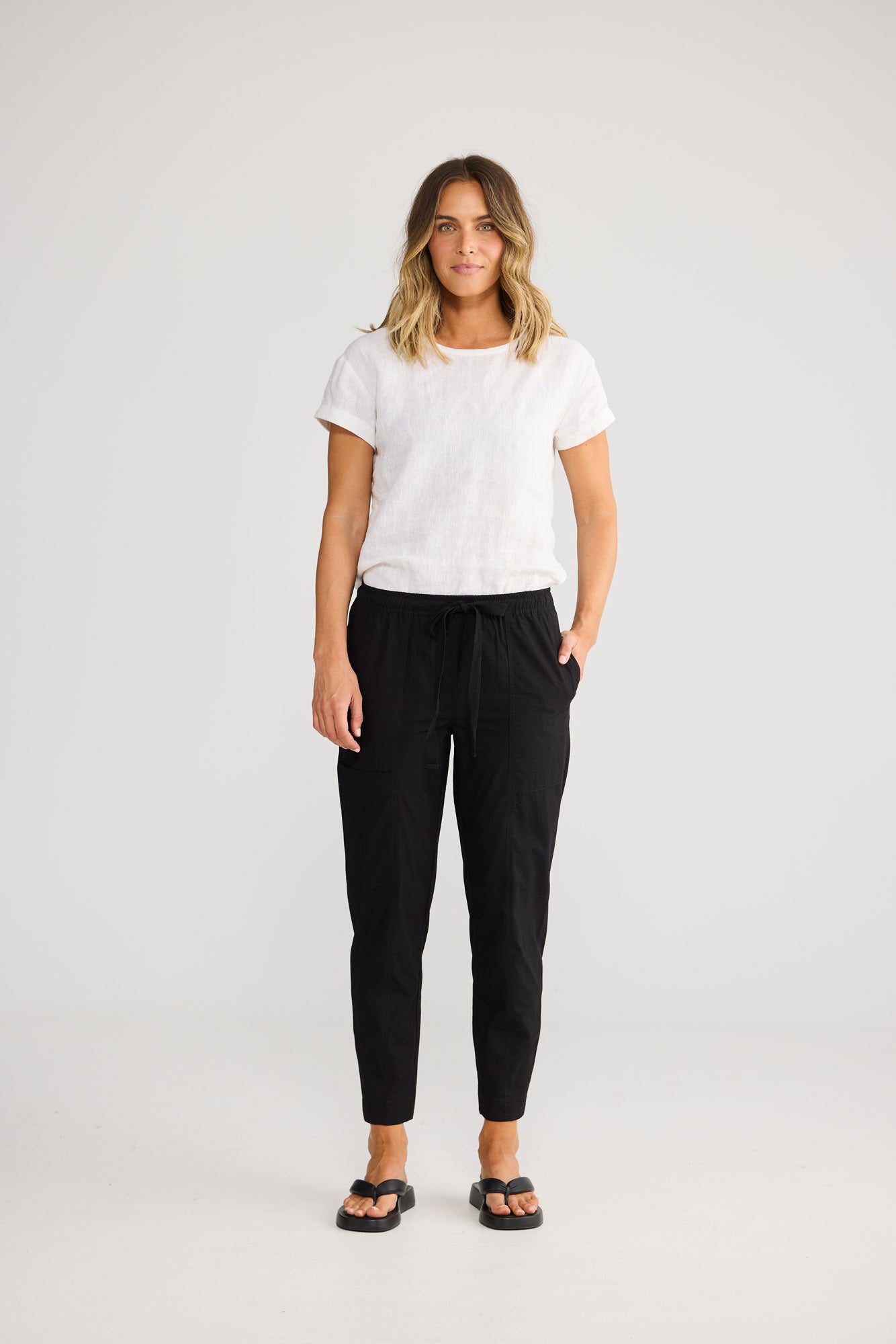 Model wearing Reva Cargo Pant in black, front view. Tie waistband, cargo-style pockets.
