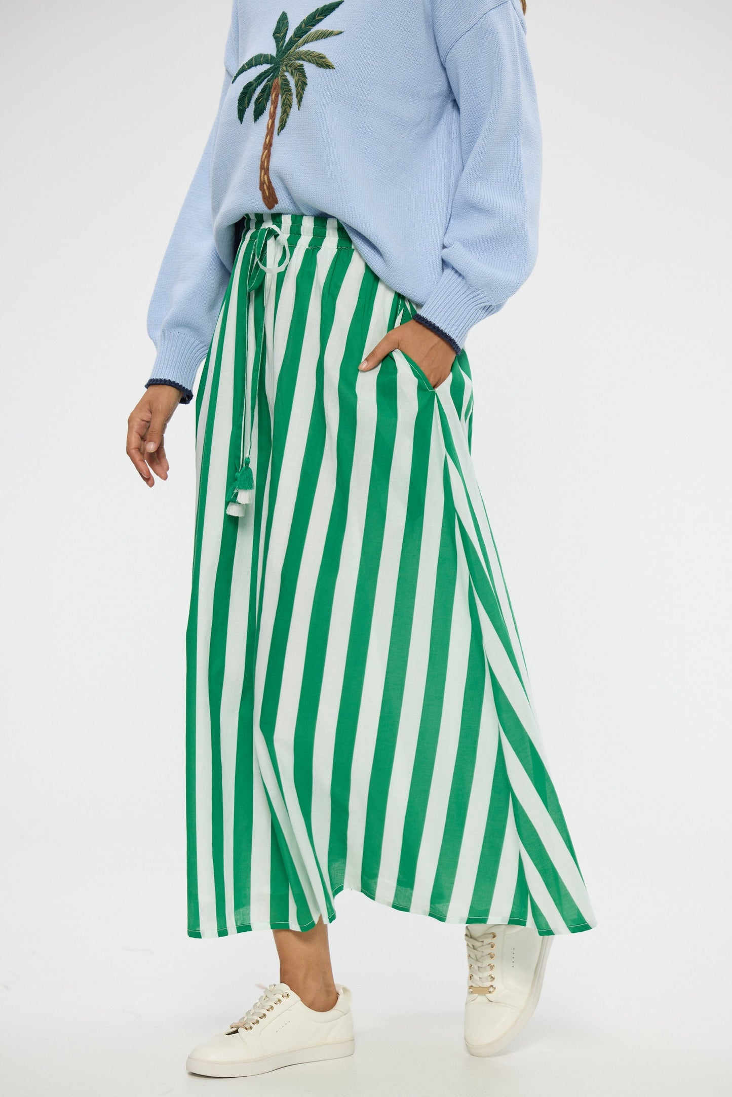 Person wearing a light blue sweatshirt with a palm tree design and green and white striped pants on a white background