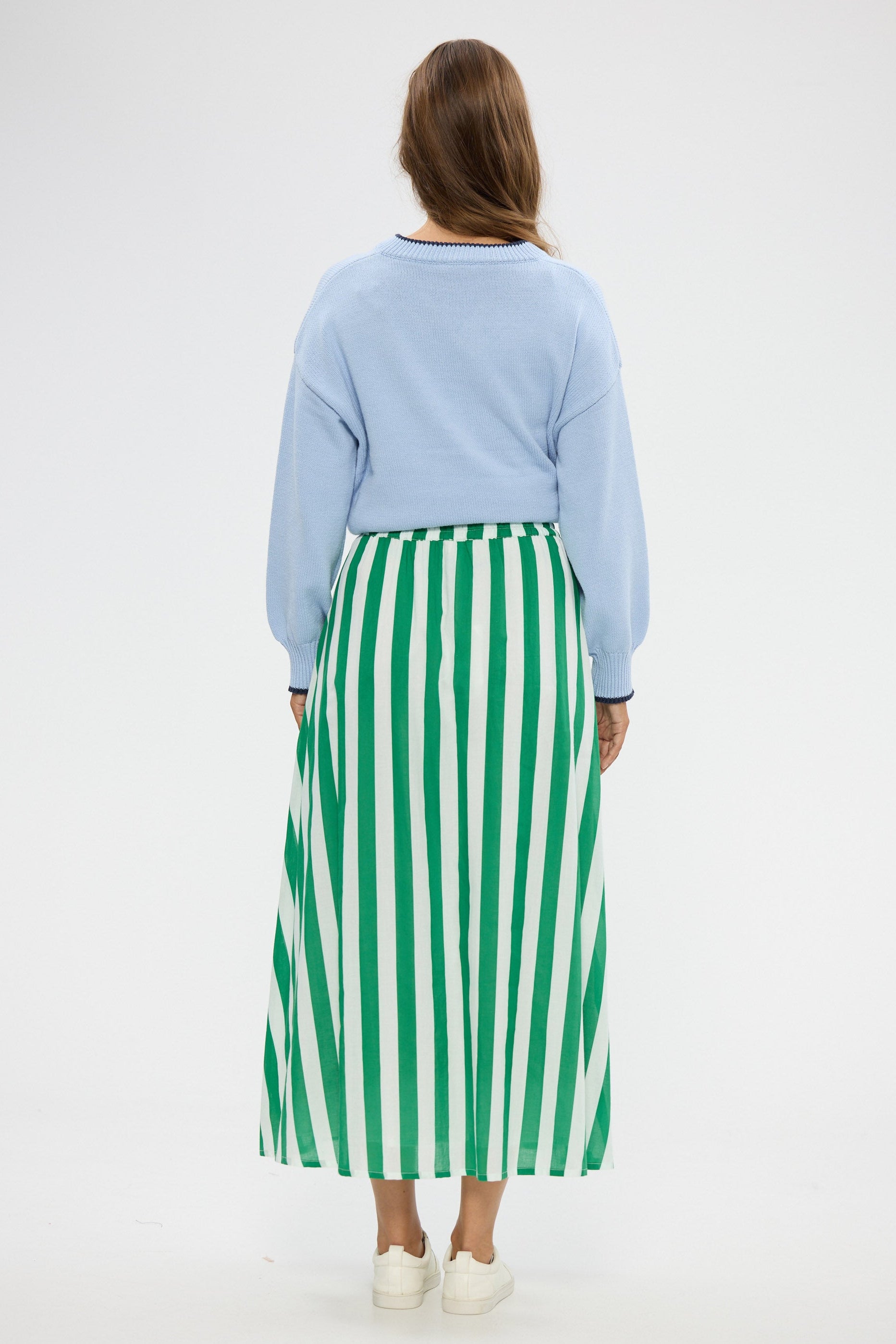 Woman wearing a light blue sweater and green and white striped skirt on a white background
