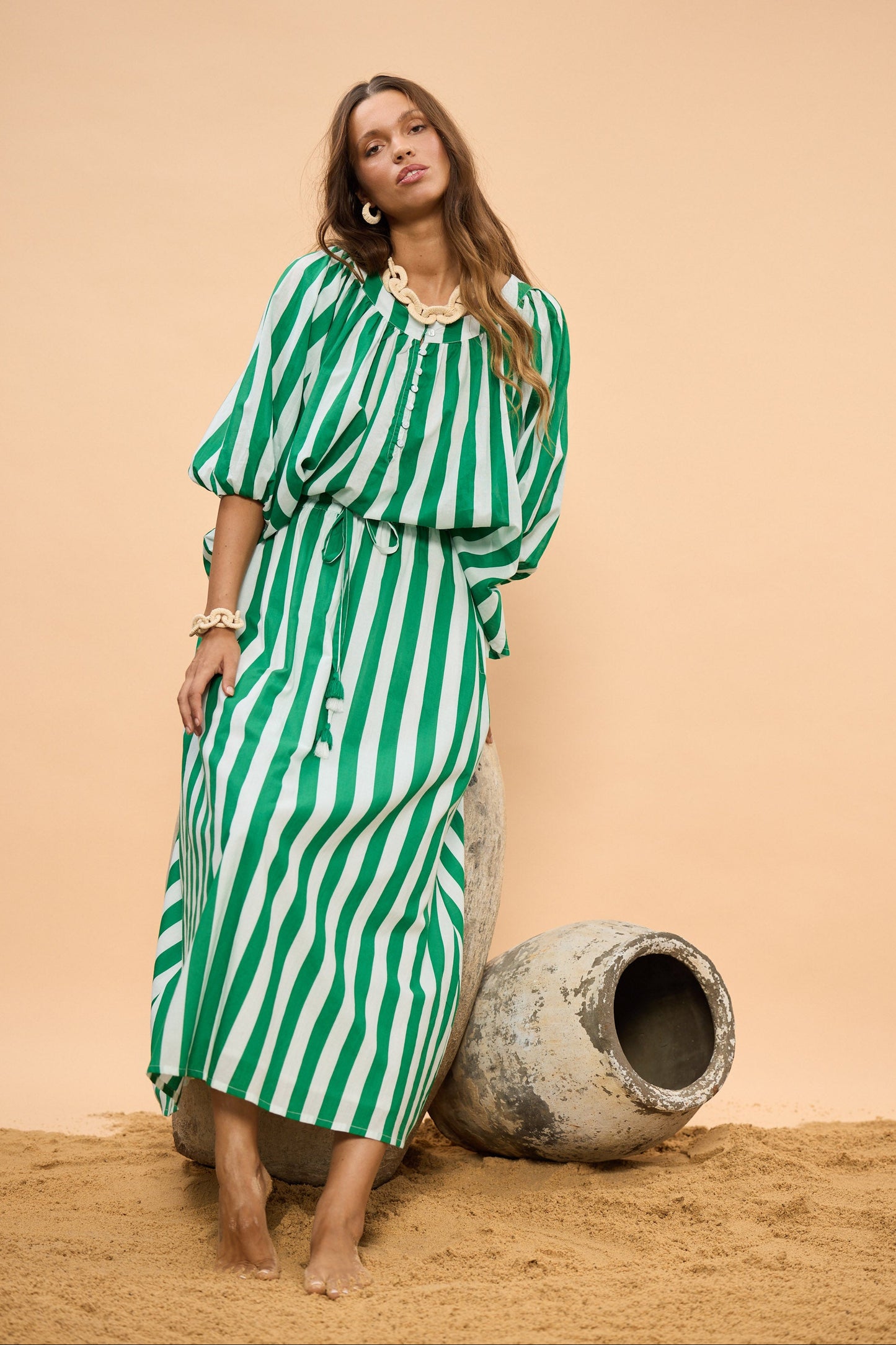 Woman in a green and white striped top and skirt standing next to large pots against a beige background