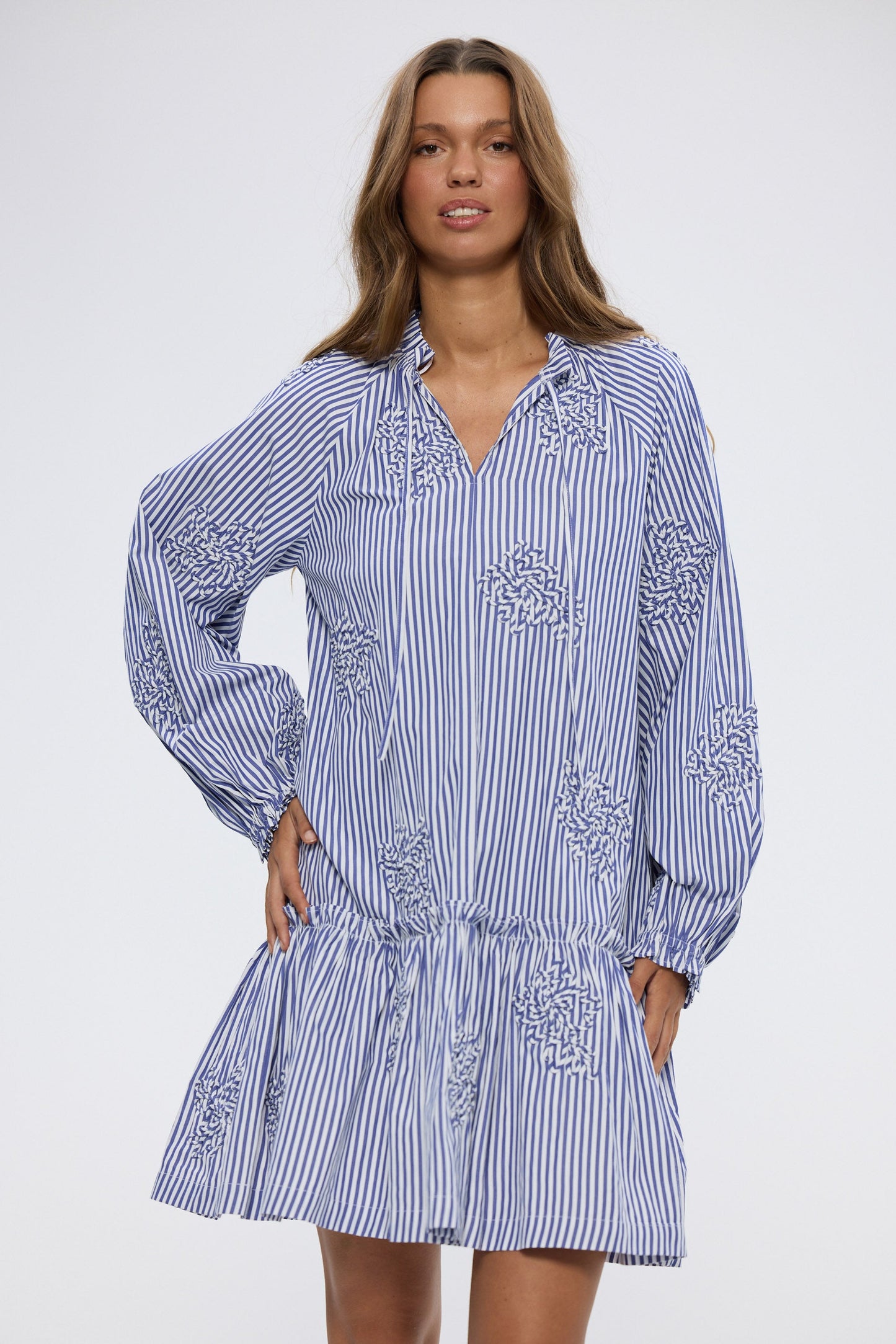 Woman wearing a blue and white striped dress with embroidery on a white background
