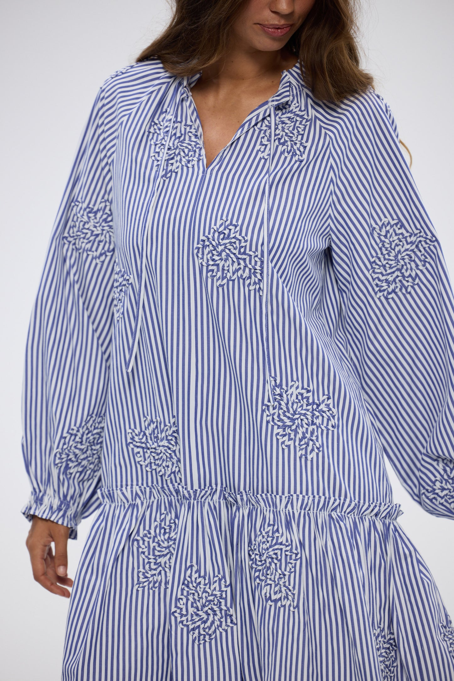 Woman wearing a blue and white striped dress with floral embroidery on a white background