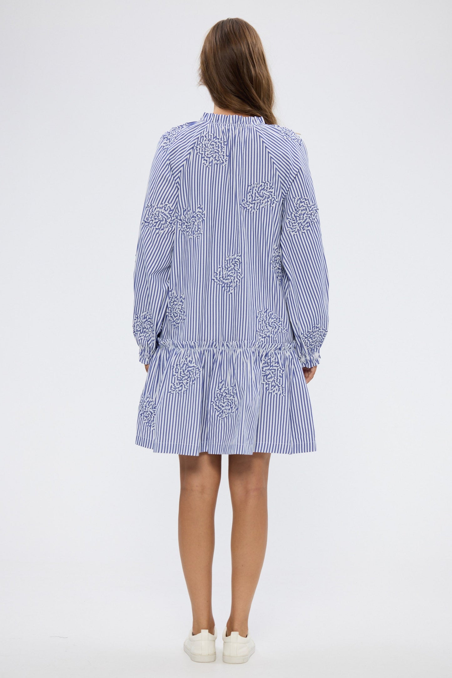 Woman wearing a blue and white striped dress with floral embroidery on a white background