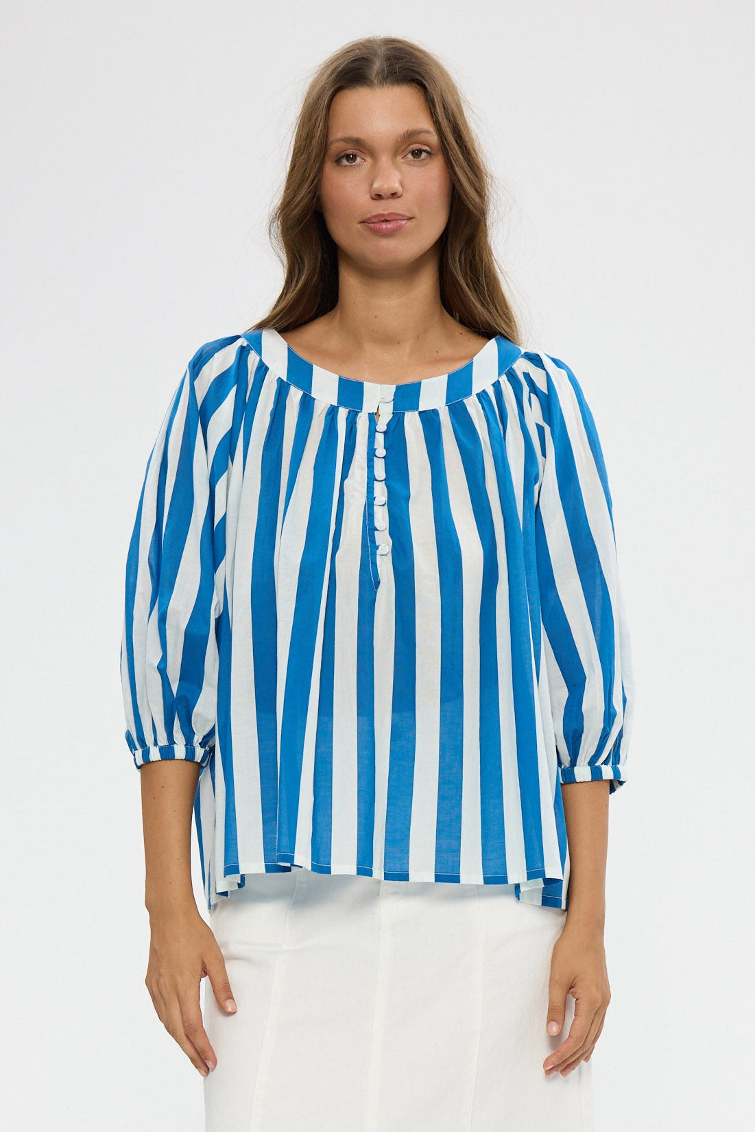 Woman wearing a blue and white striped shirt with white pants on a white background