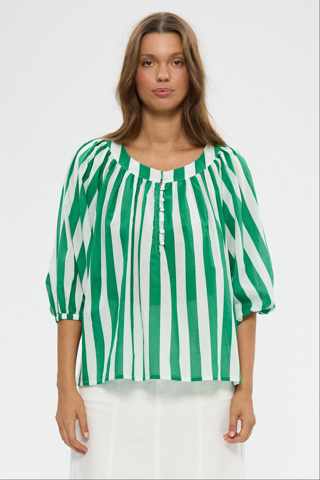 Woman wearing a green and white striped blouse with white pants on a white background