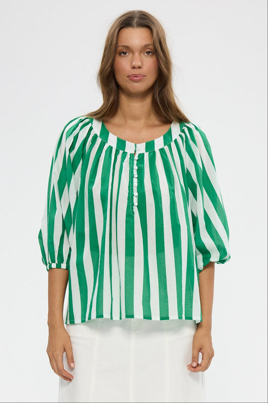 Woman wearing a green and white striped blouse with white pants on a white background