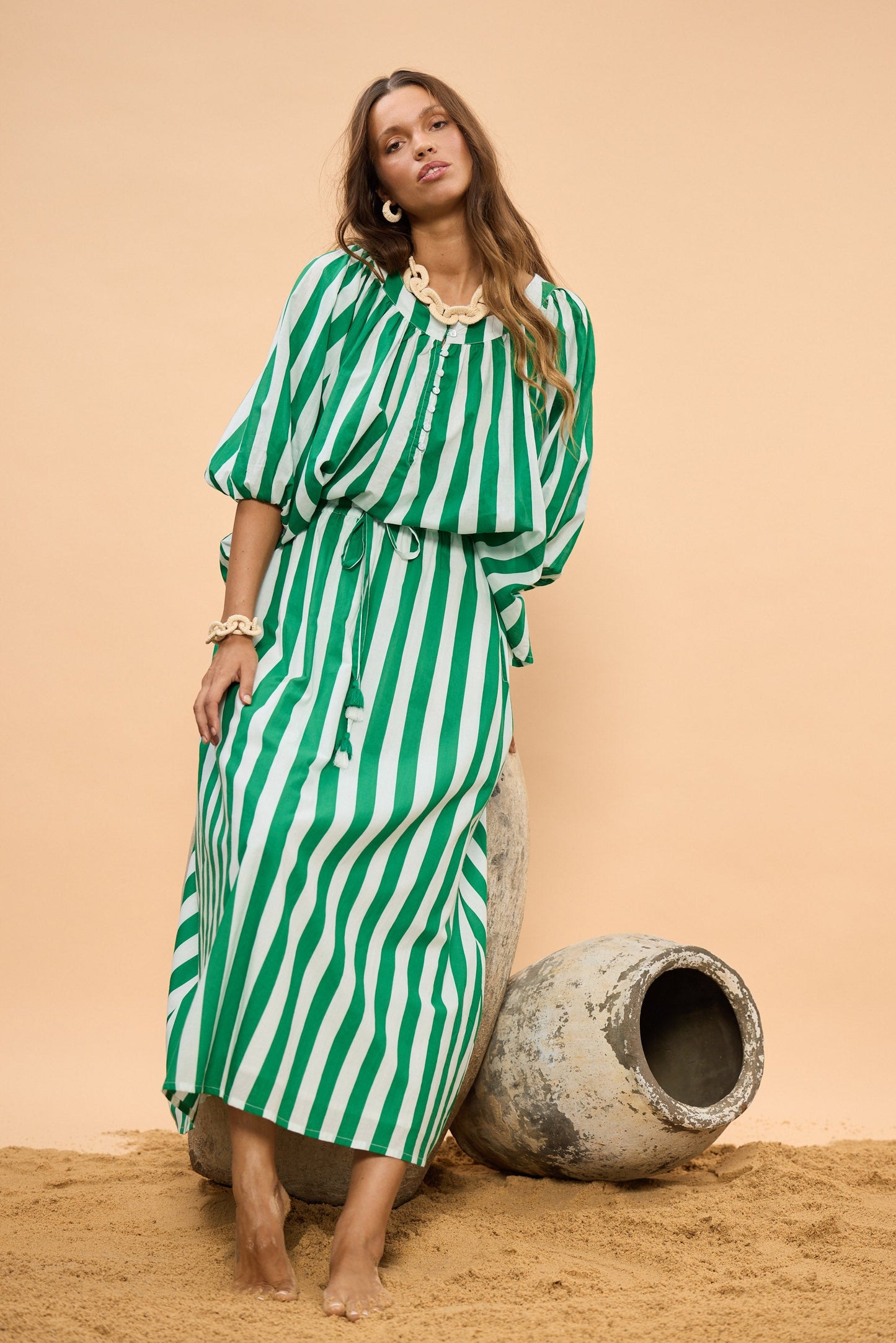 Woman in a green and white striped top and skirt standing next to large stones against a beige background