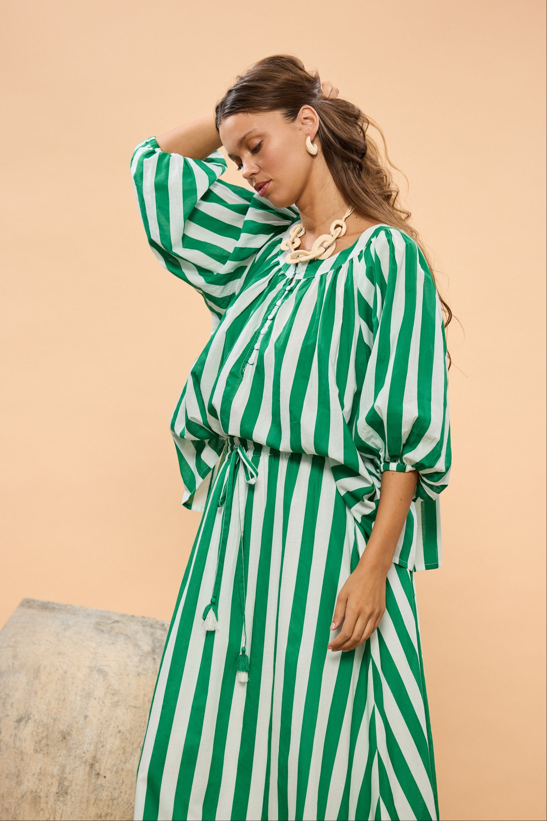 Woman wearing a green and white striped top and skirt against a beige background